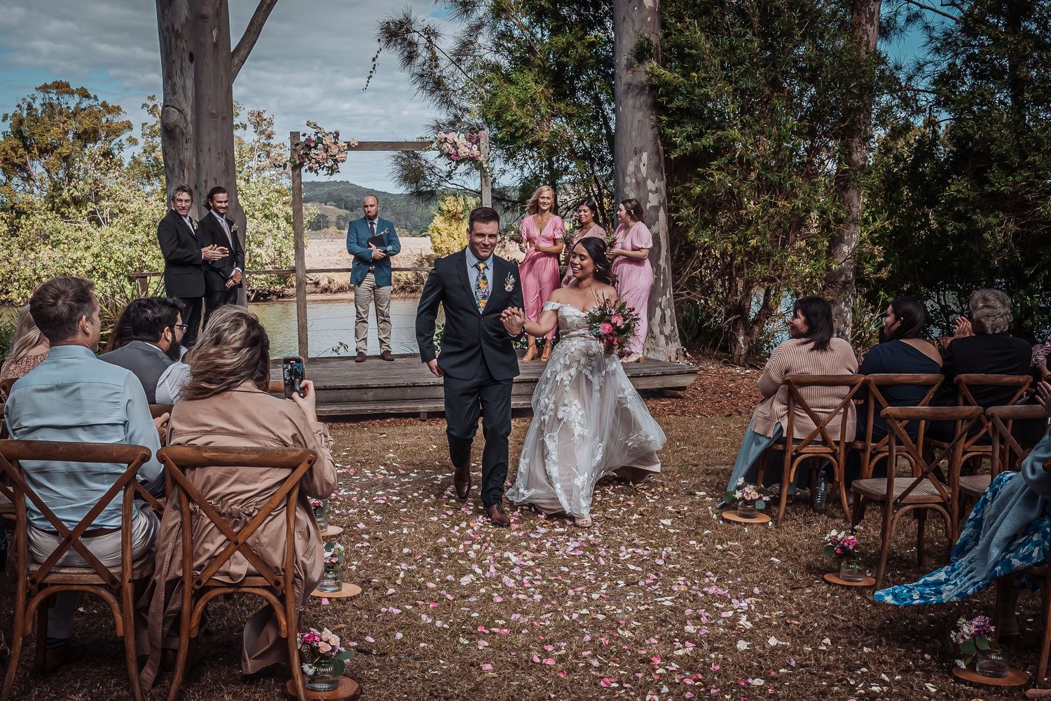 Outdoor wedding ceremony in a rustic forest setting with wooden chairs and natural surroundings.