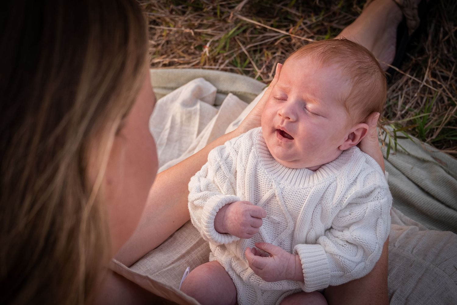 Baby wearing white sweater laughs joyfully during outdoor portrait session.
