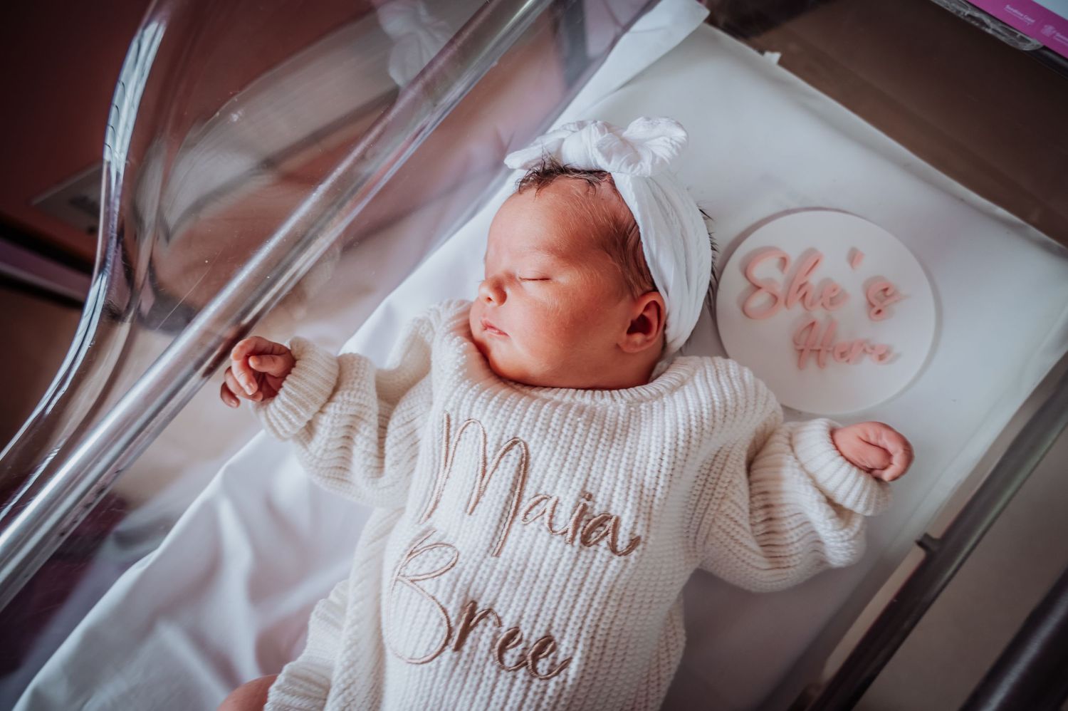 A sleeping newborn in a cozy white knitted outfit with a bow headband.