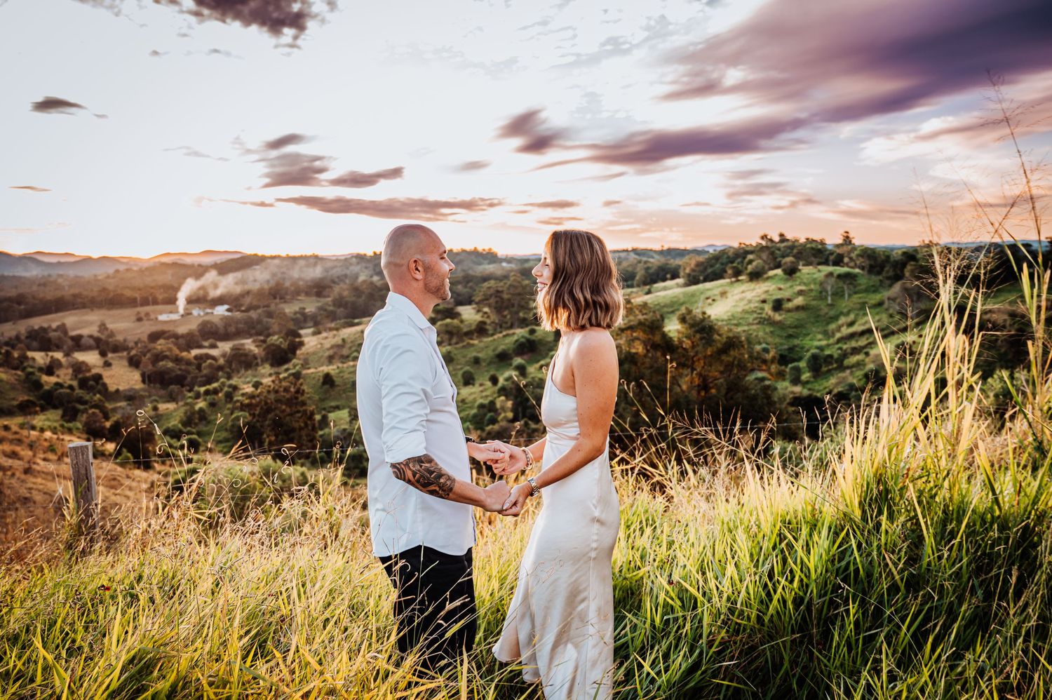 A couple holds hands while standing on a hilltop during golden hour.