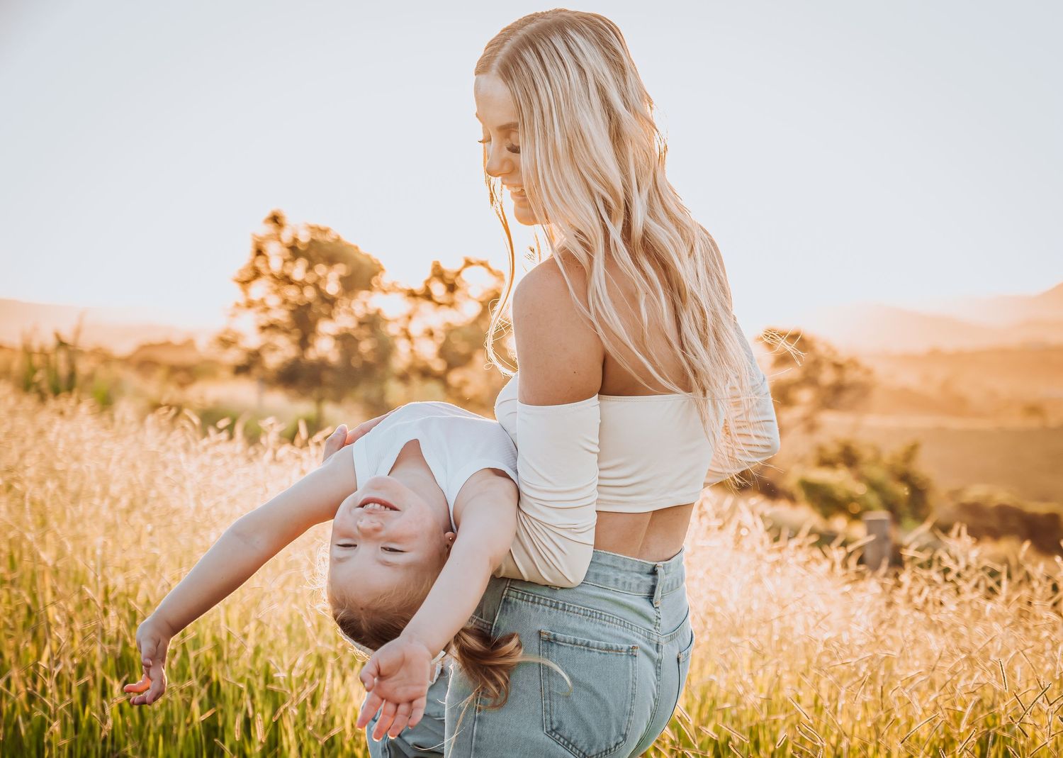 Outdoor portrait in a field with person holding child upside down playfully.