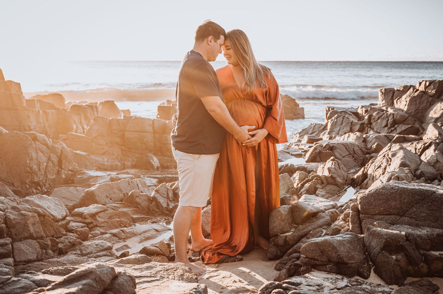 Romantic coastal maternity portrait among rocky outcrops at golden hour.
