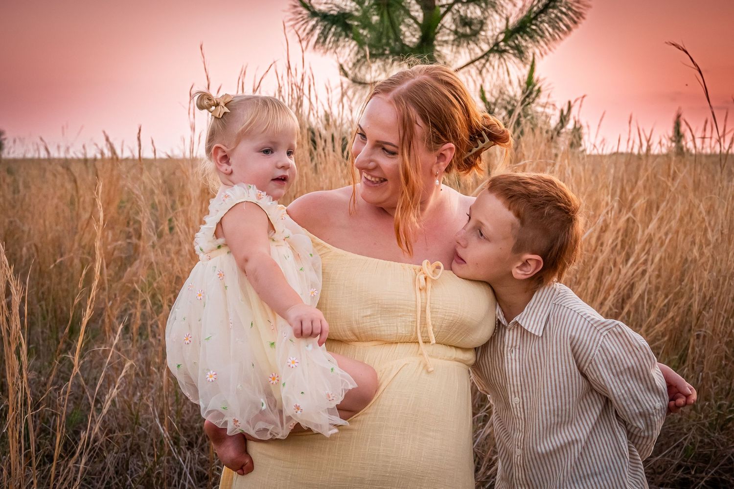 A tender family moment captured in a field during golden hour with children in light colored outfits.