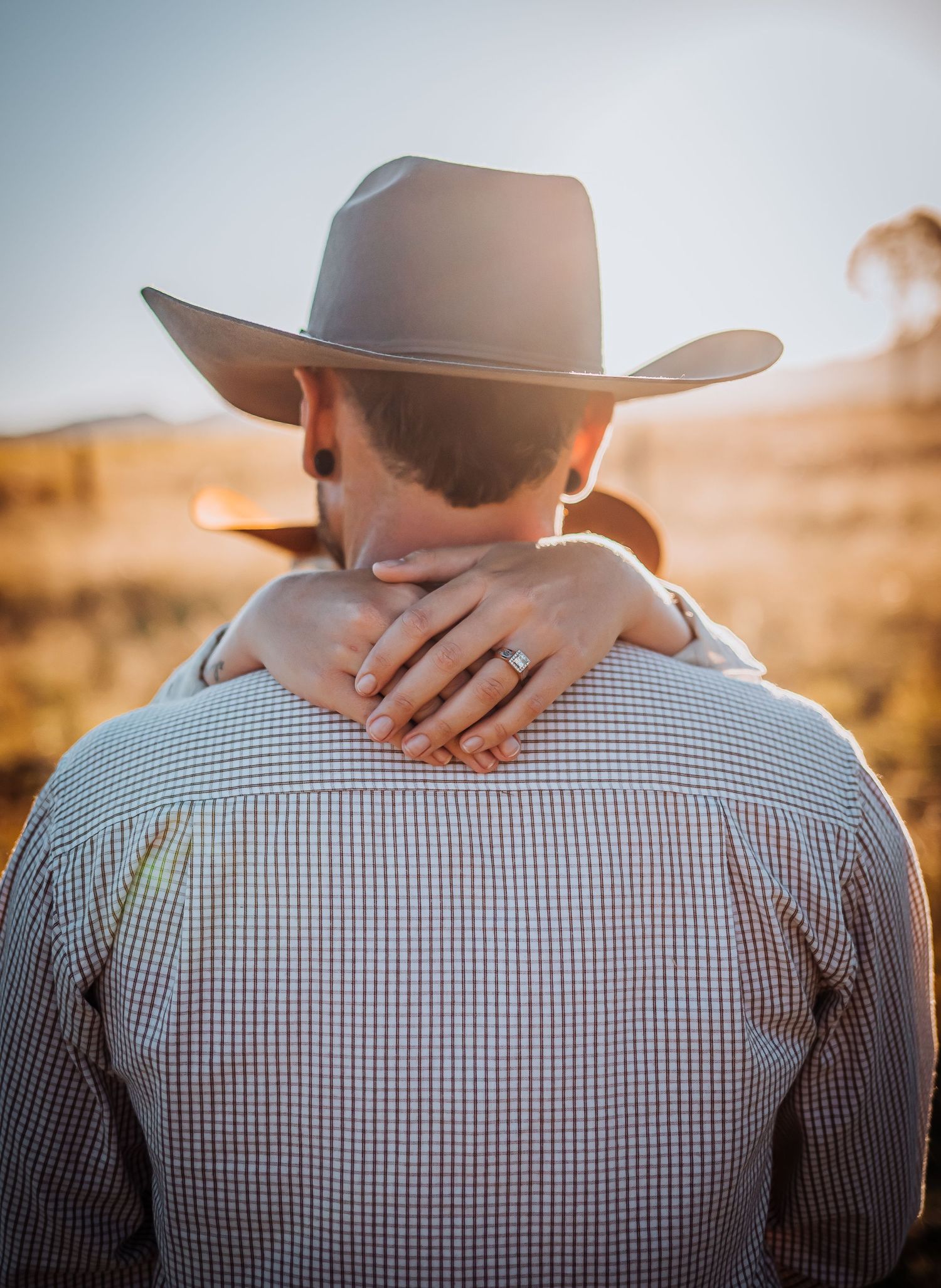 Back view of someone in a checkered shirt and cowboy hat with arms wrapped around their neck.