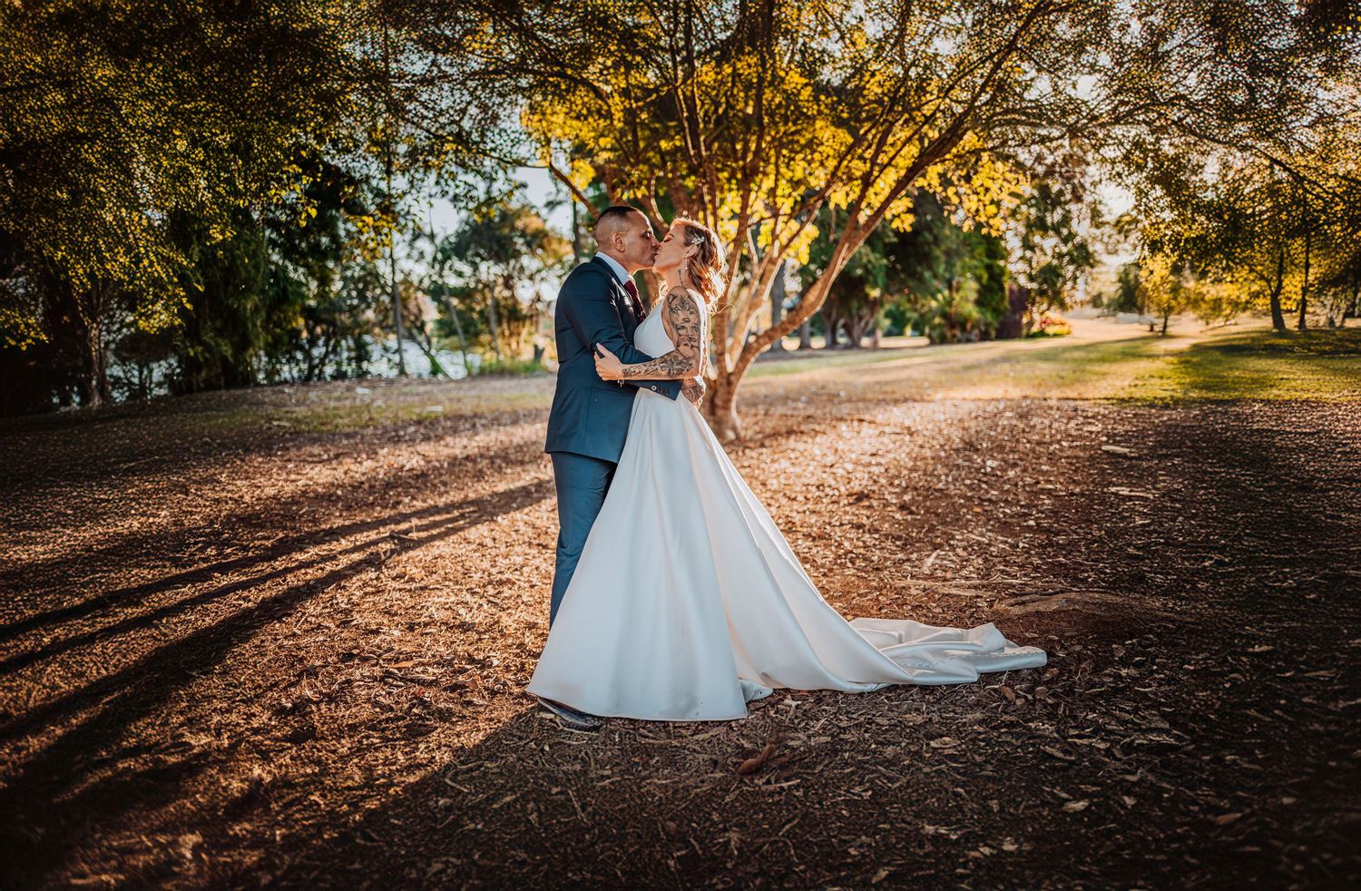Bride and groom dance together on tree-lined path at golden hour.