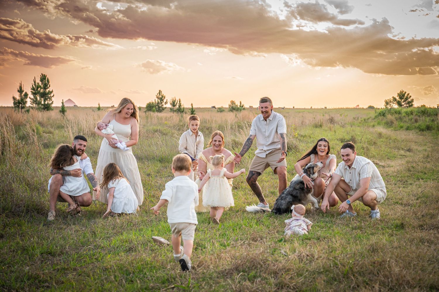 Large family gathering in field during golden sunset with children playing.