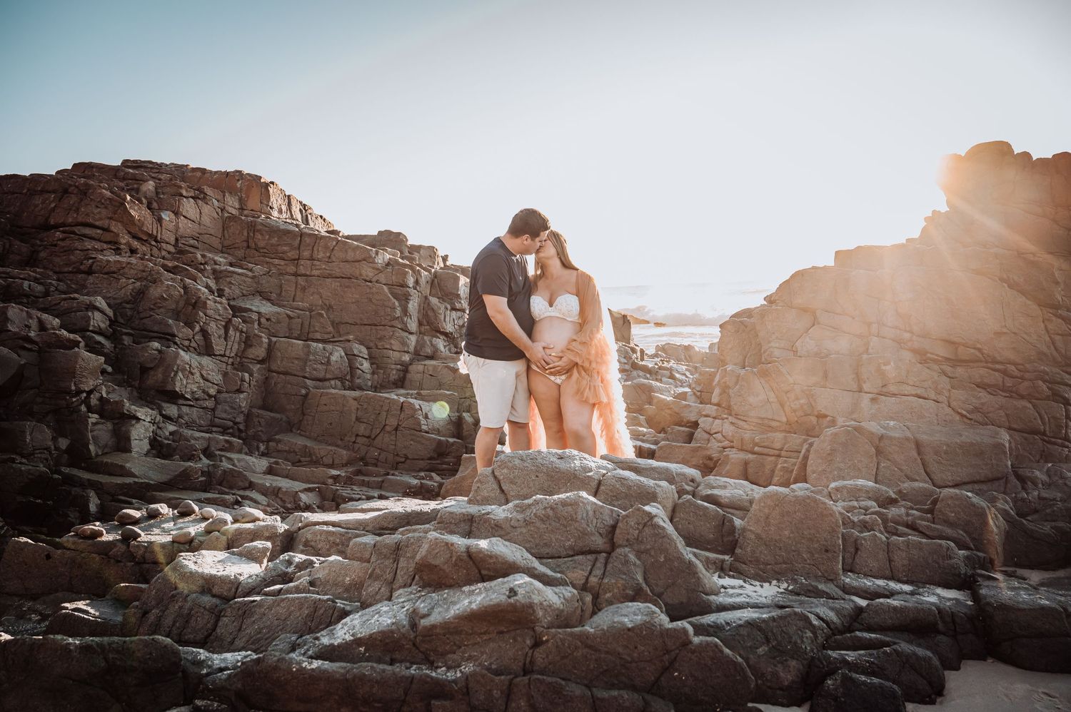 Sunset maternity photoshoot on dramatic rocky cliffs by the ocean.