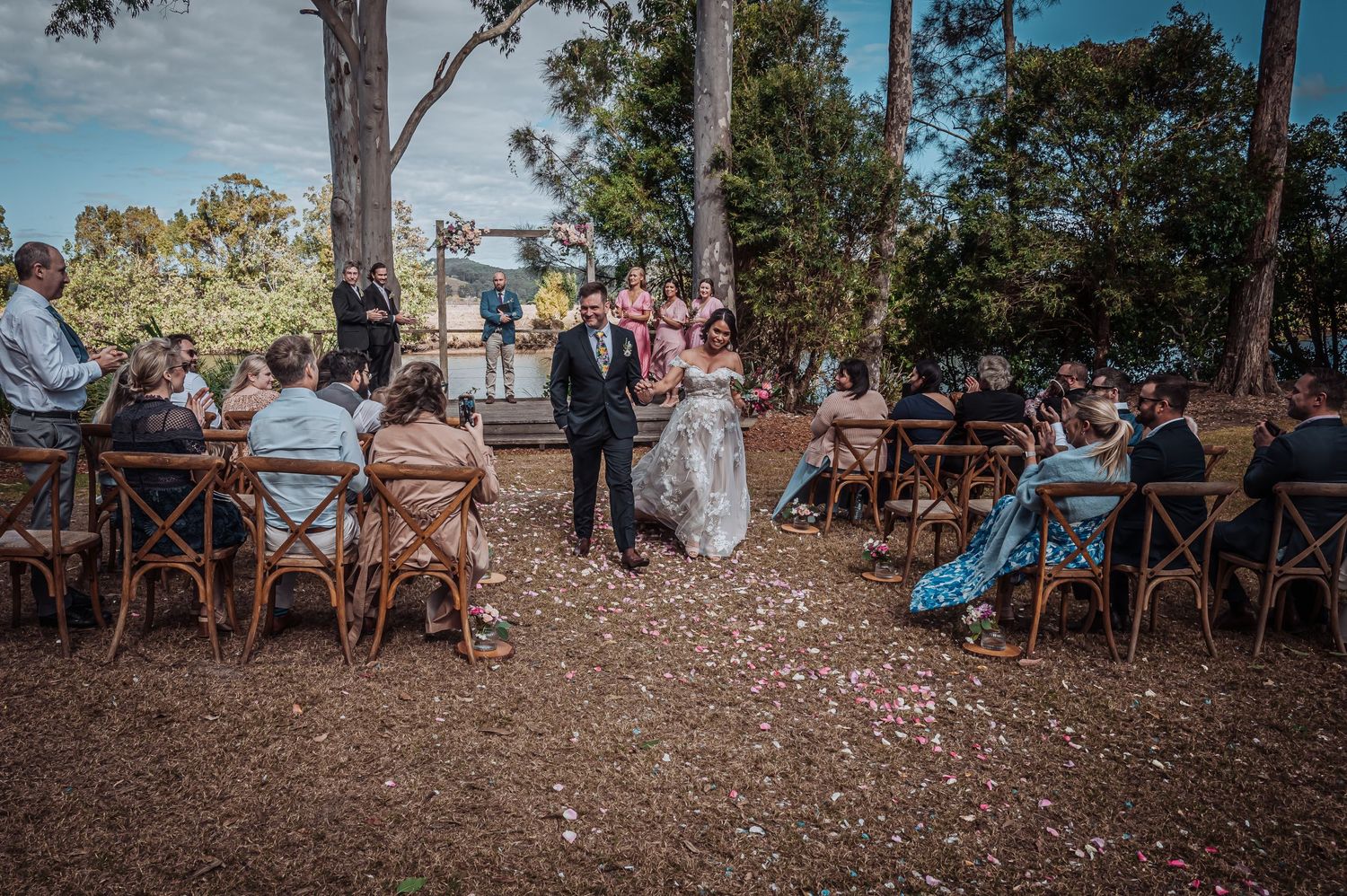 Intimate forest wedding ceremony with guests seated on wooden chairs under tall eucalyptus trees.