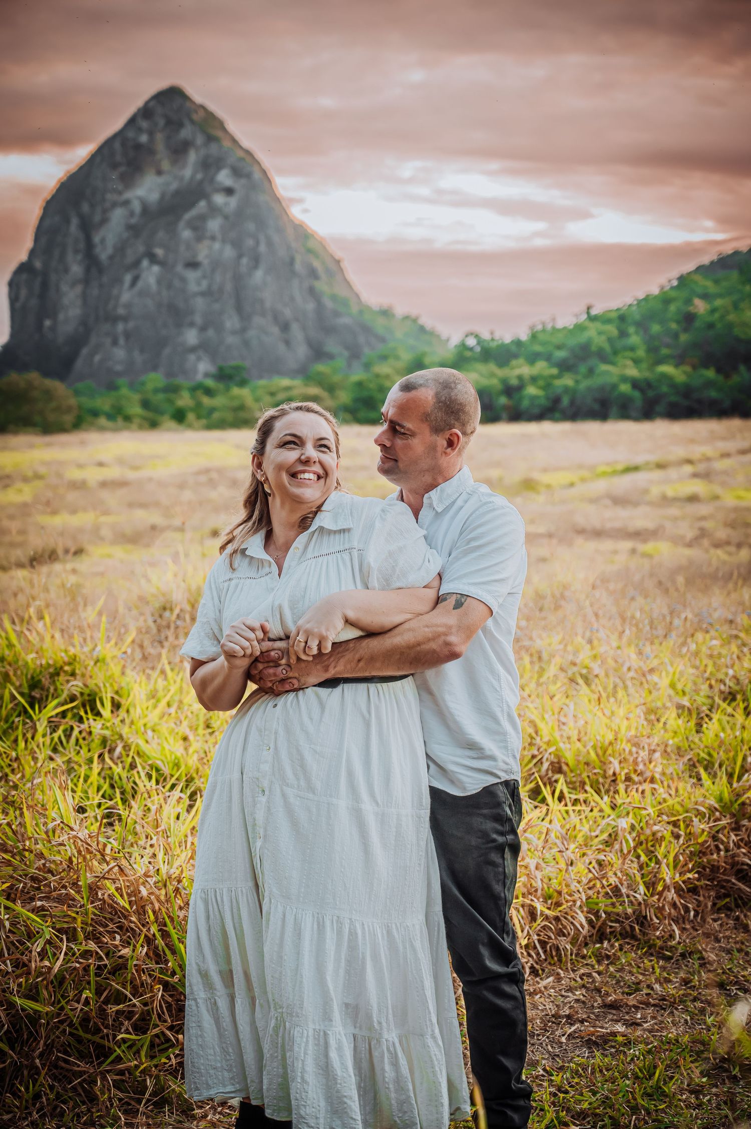 A couple shares a joyful moment in front of a dramatic mountain landscape during sunset.