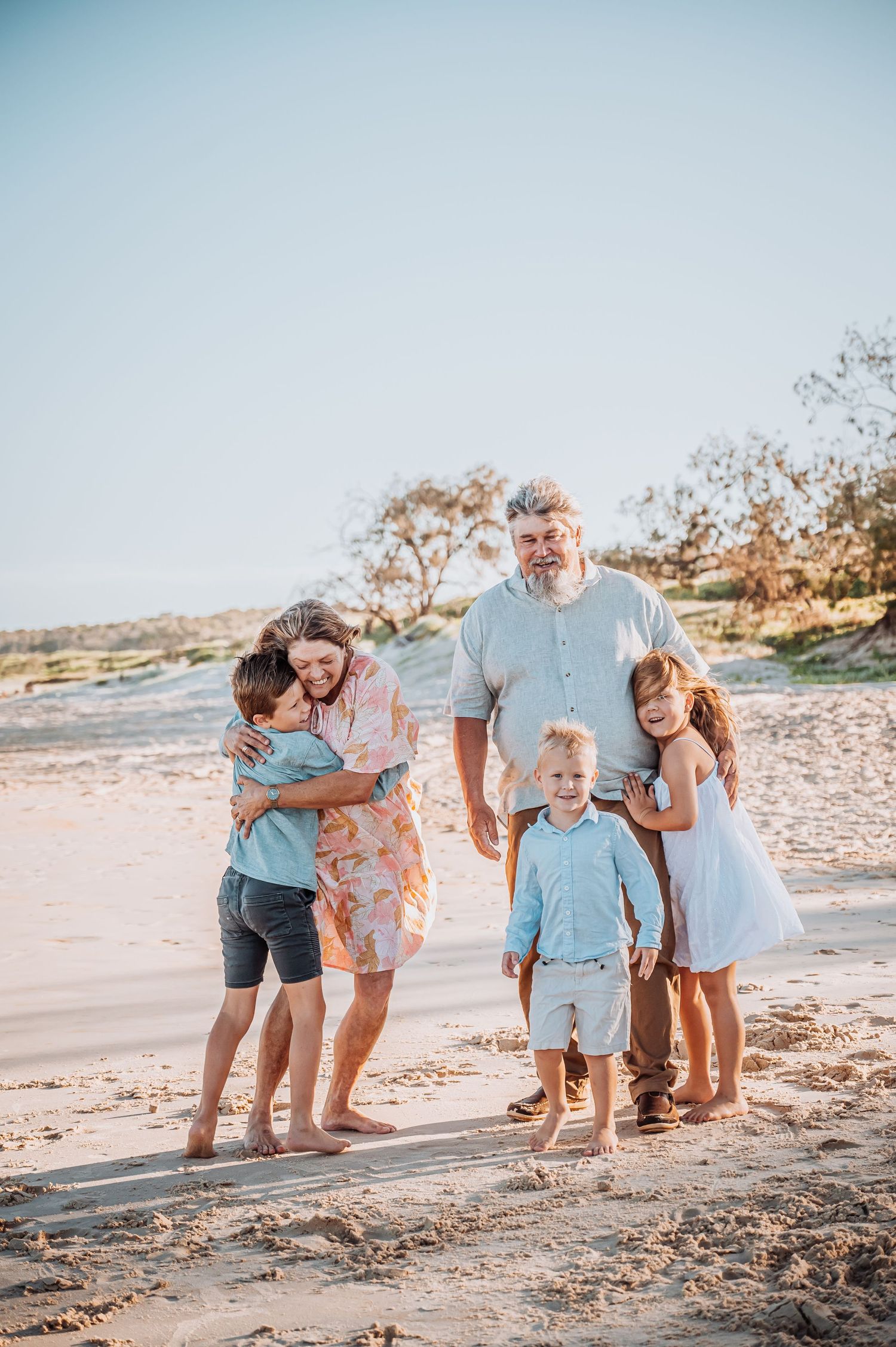 Group poses for a casual beach photo while wearing light summer clothing at golden hour.