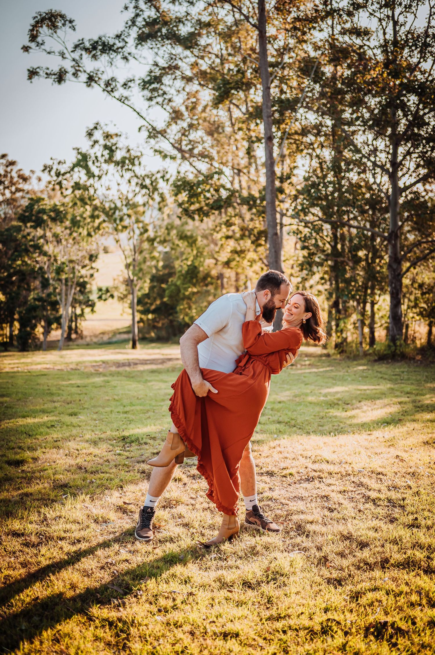 A romantic dip pose captured in warm evening sunlight on grassy terrain.