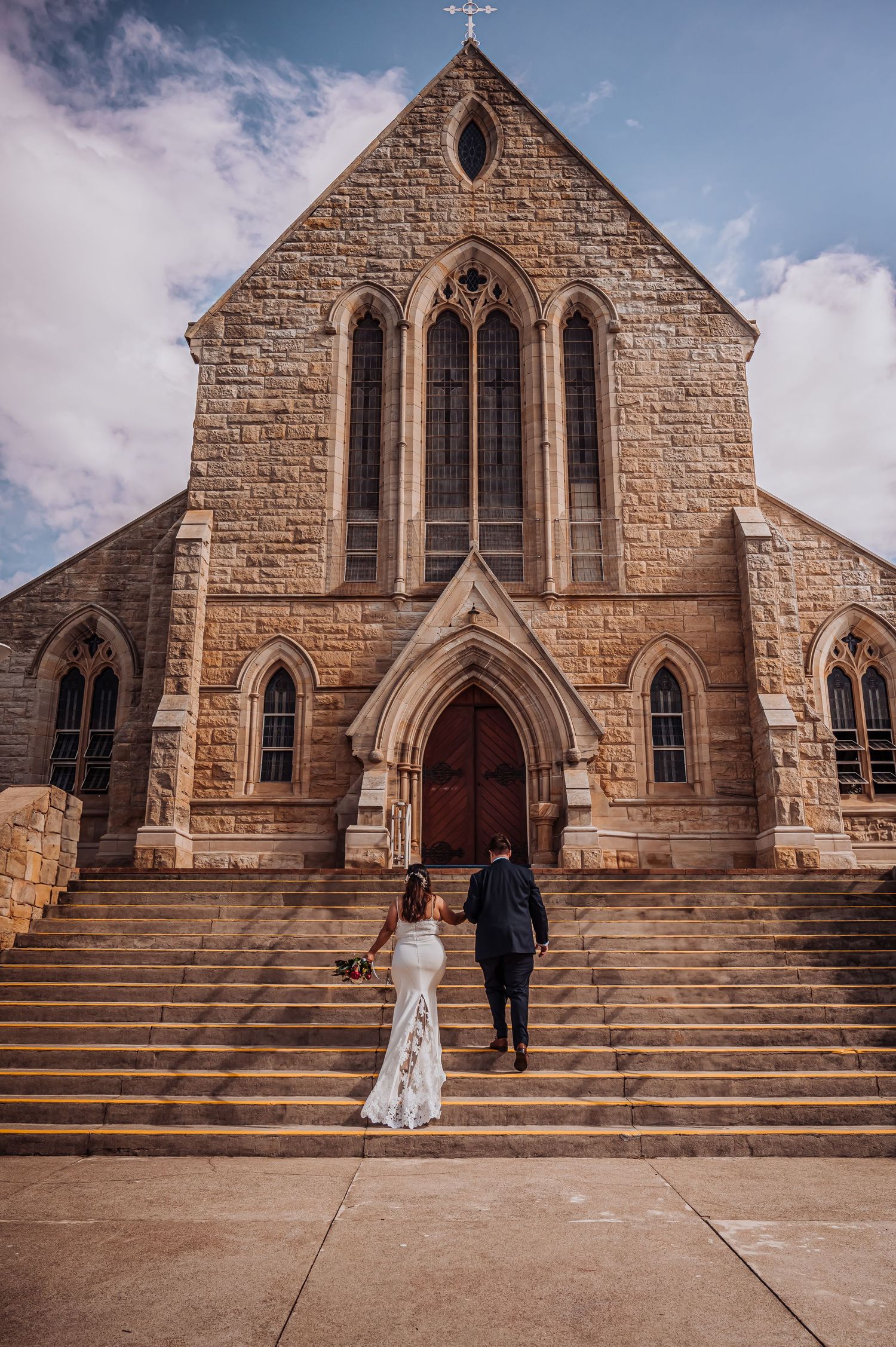 Classic stone church exterior with couple ascending grand steps during golden hour ceremony.