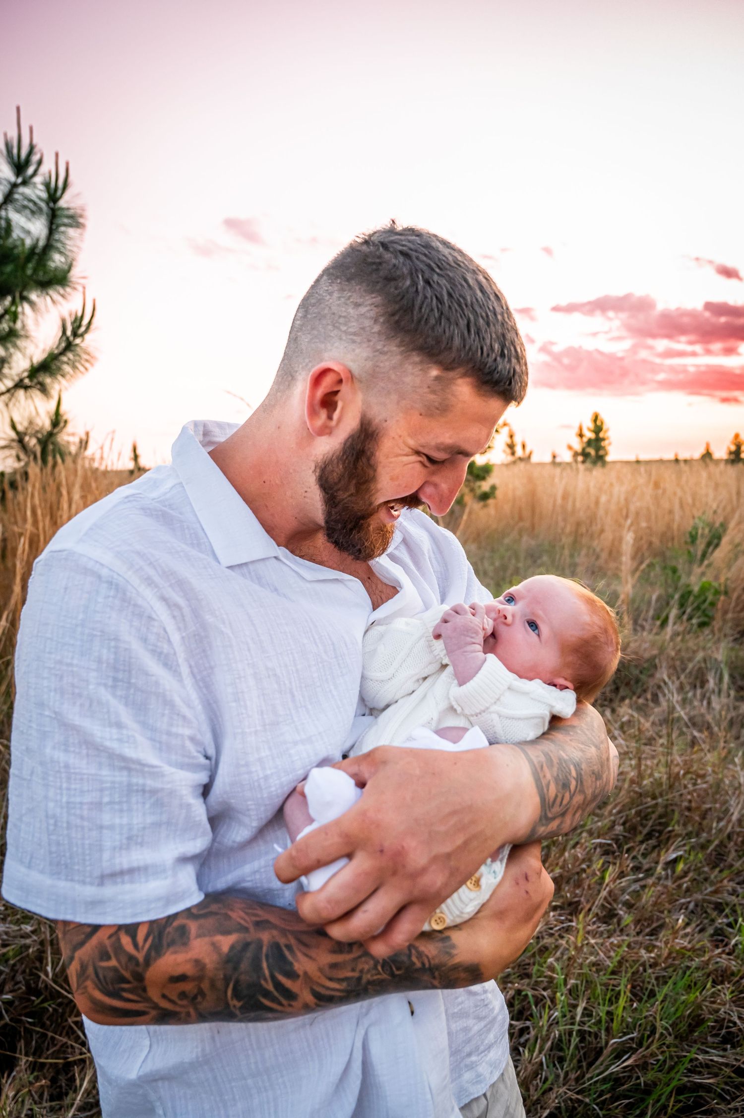 A sweet outdoor portrait showing a parent cradling a small baby at sunset among tall grasses.