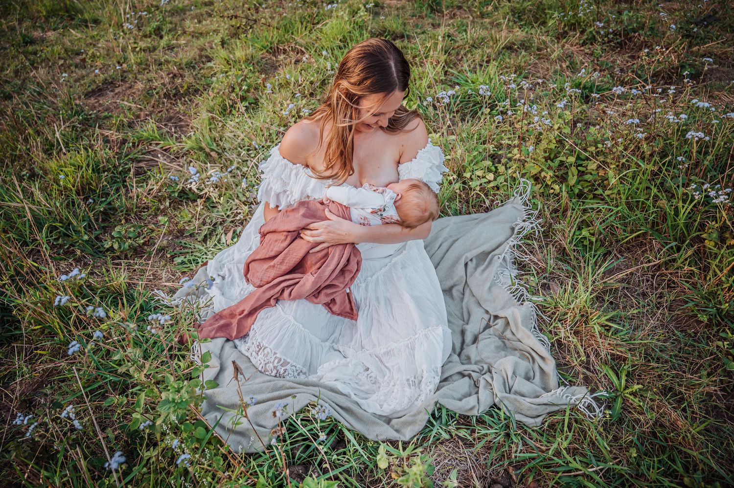 Intimate outdoor portrait on blanket surrounded by wildflowers and tall grass.