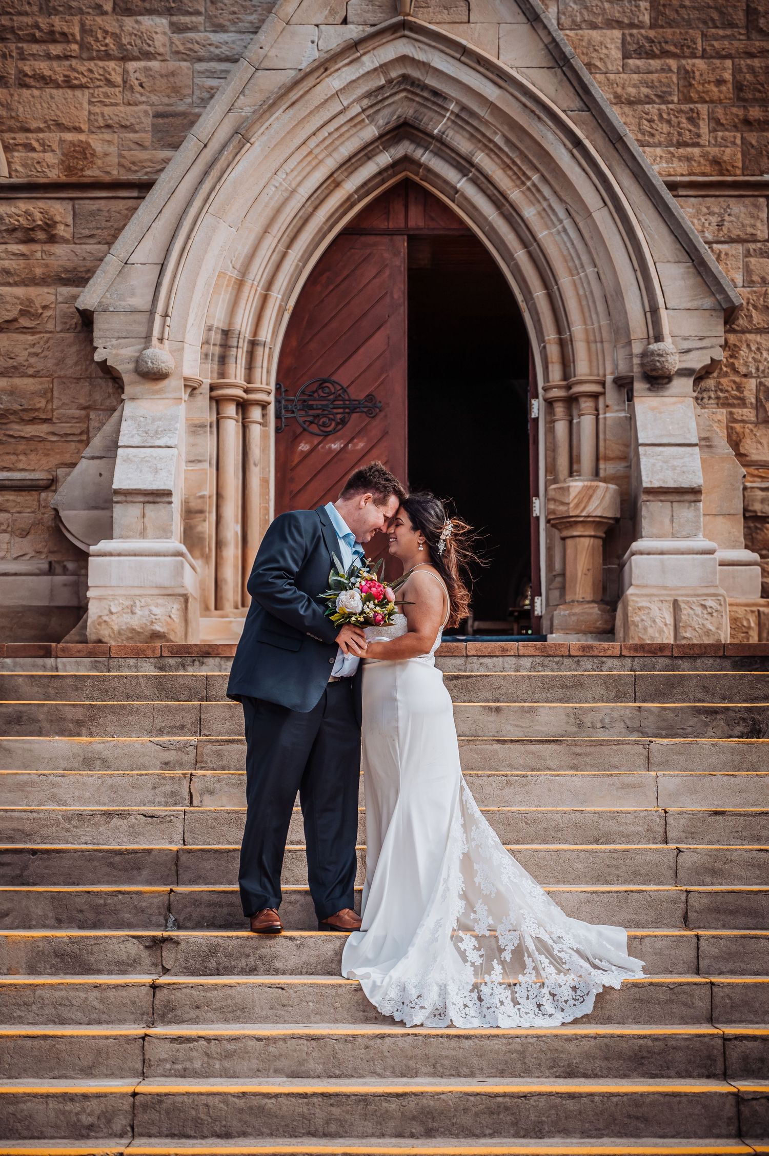 A bride and groom share an intimate moment on stone church steps.