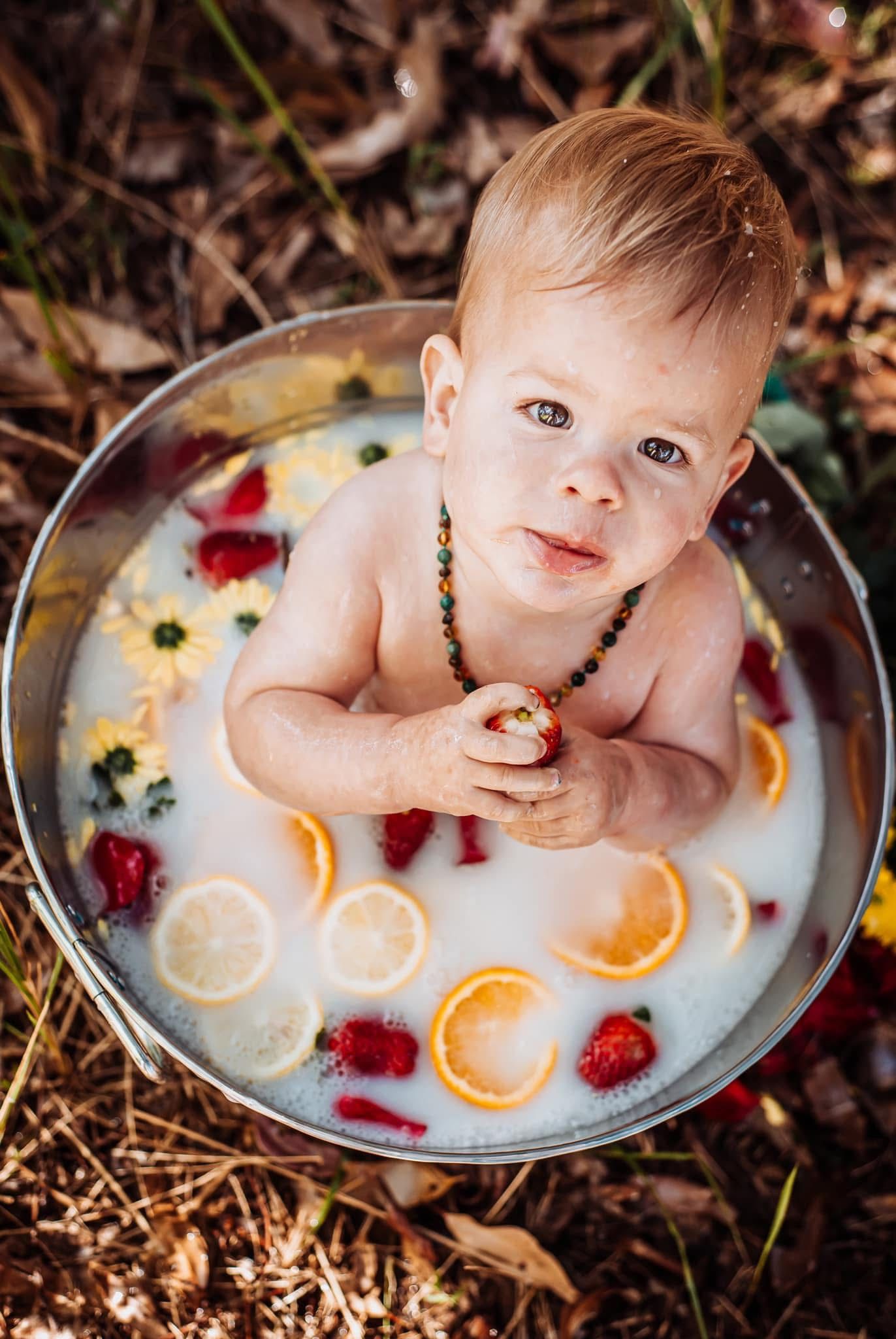 Dreamy outdoor milk bath portrait with floating oranges and red flowers.