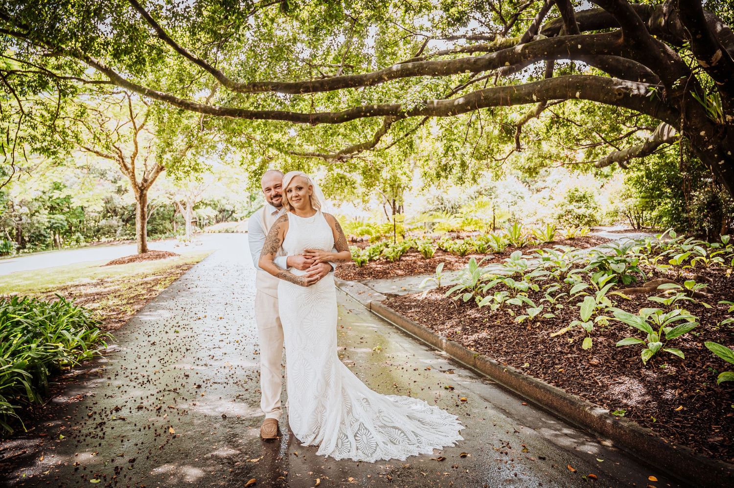 Joyful wedding moment captured on garden path under natural tree canopy.