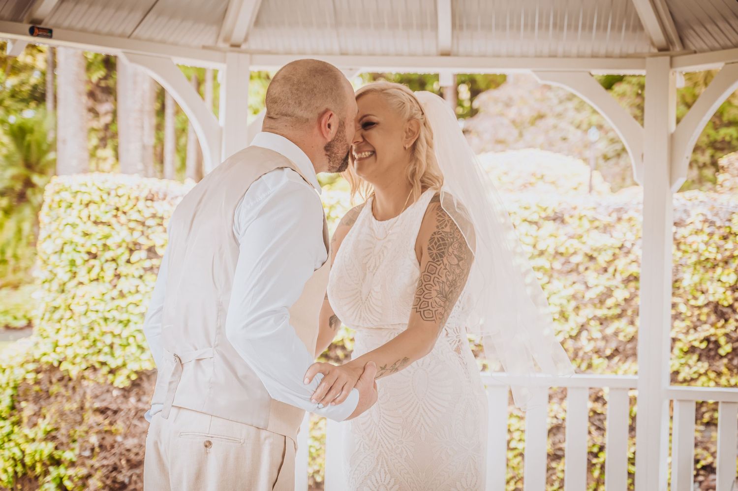 Intimate wedding ceremony moment captured in sunlit white gazebo.