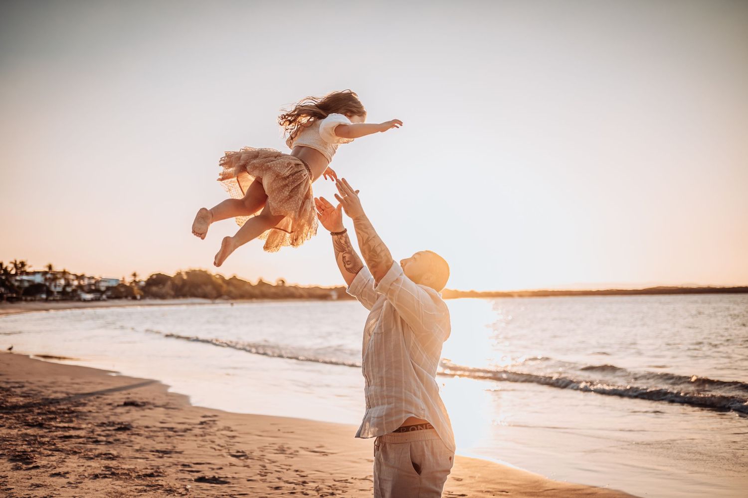 Playful moment captured on beach during golden hour with ocean waves in background.