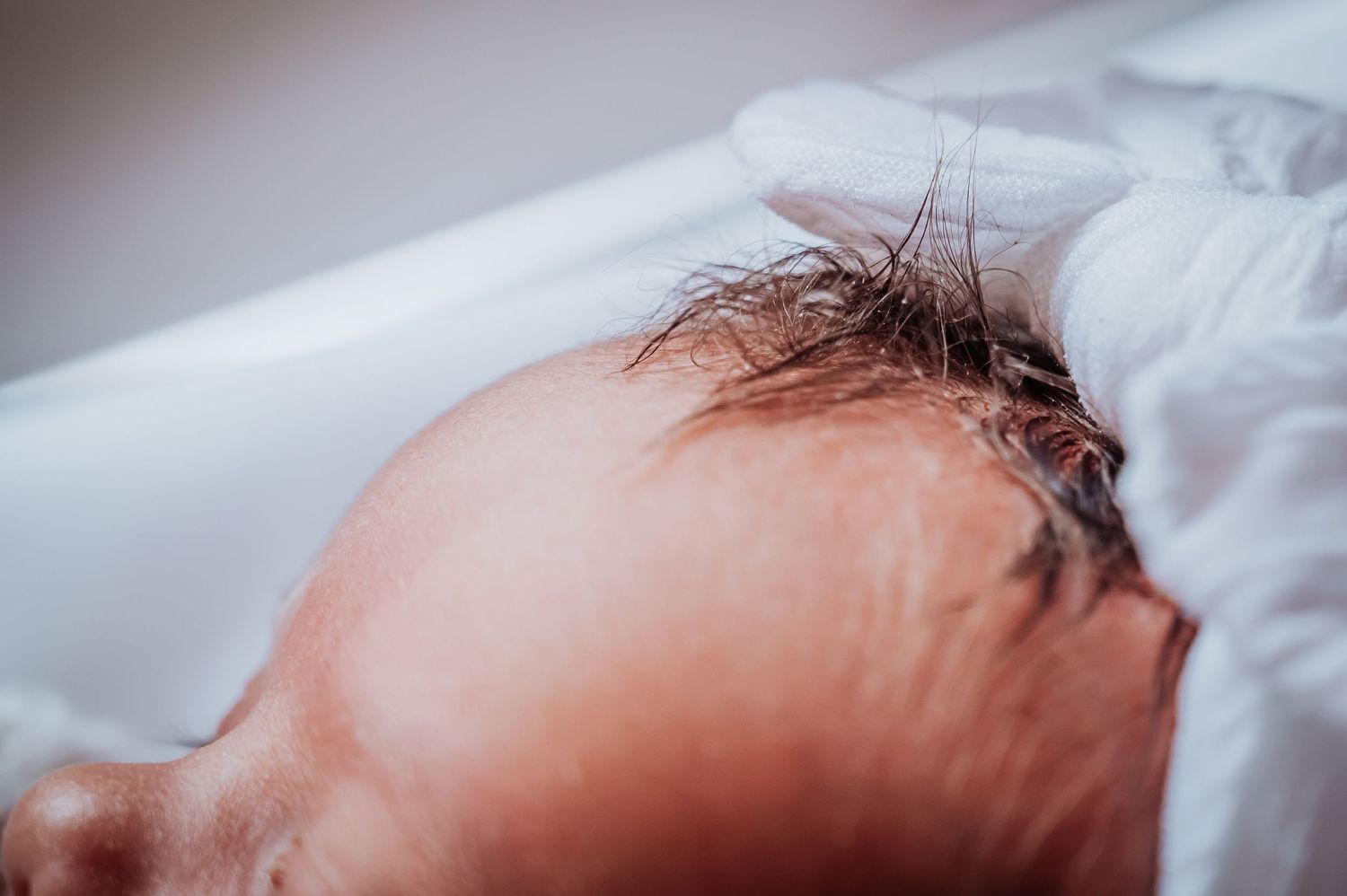Macro shot of sleeping newborn baby's head and hair against white bedding.