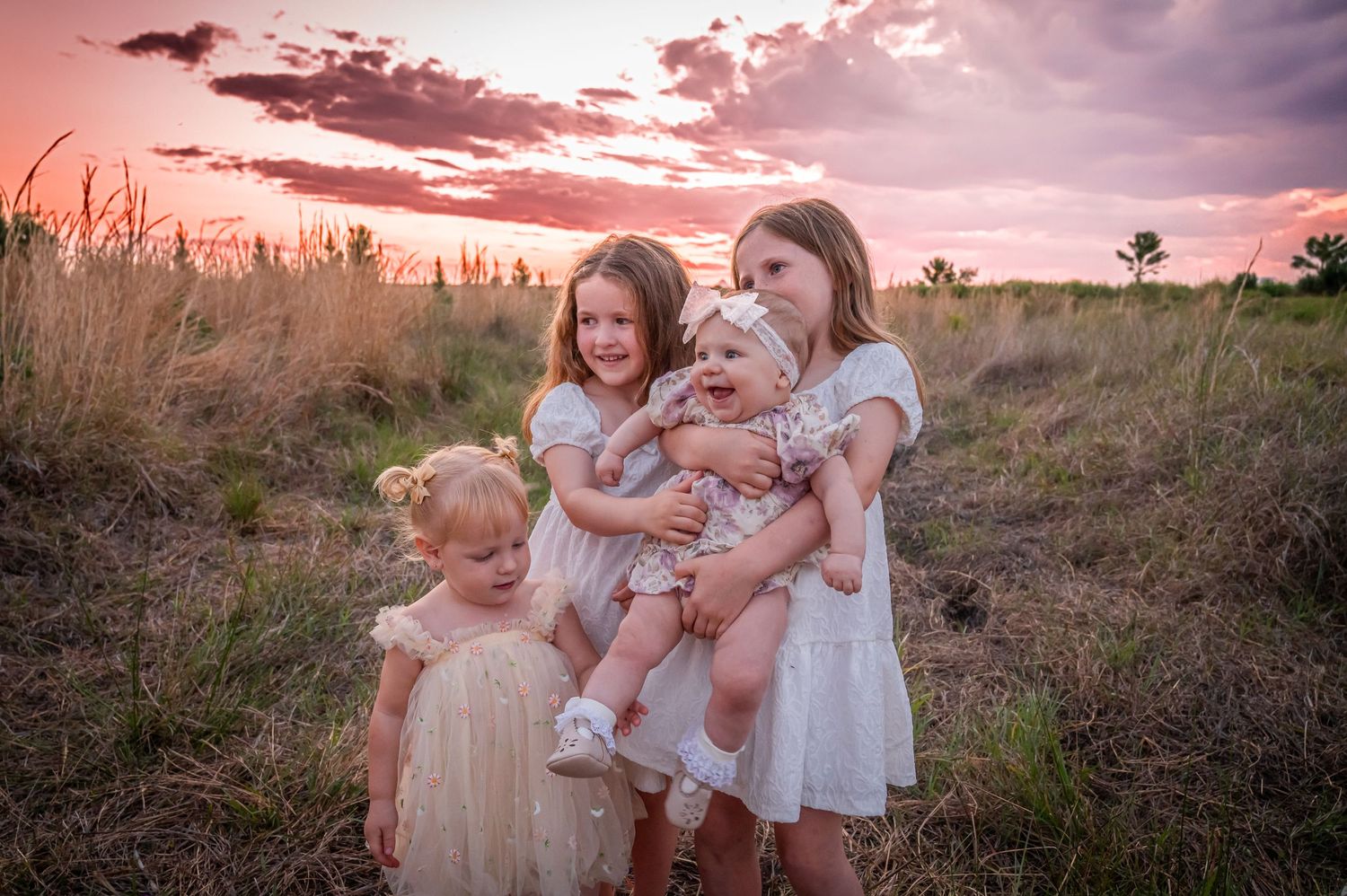A heartwarming group photo of children and adults in white dresses against a pink sunset sky.