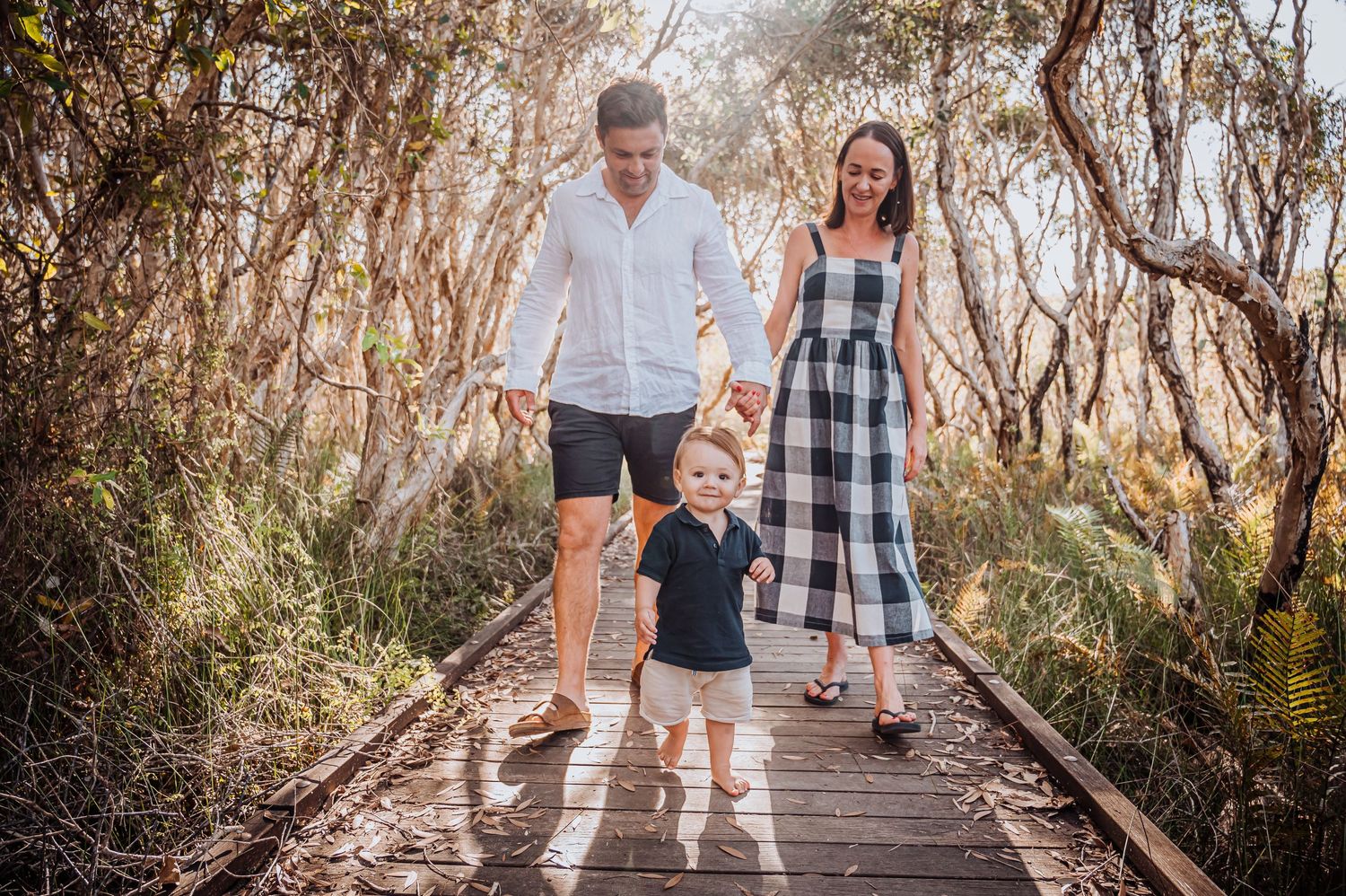 A family walks together holding hands on a wooden boardwalk through natural scenery.