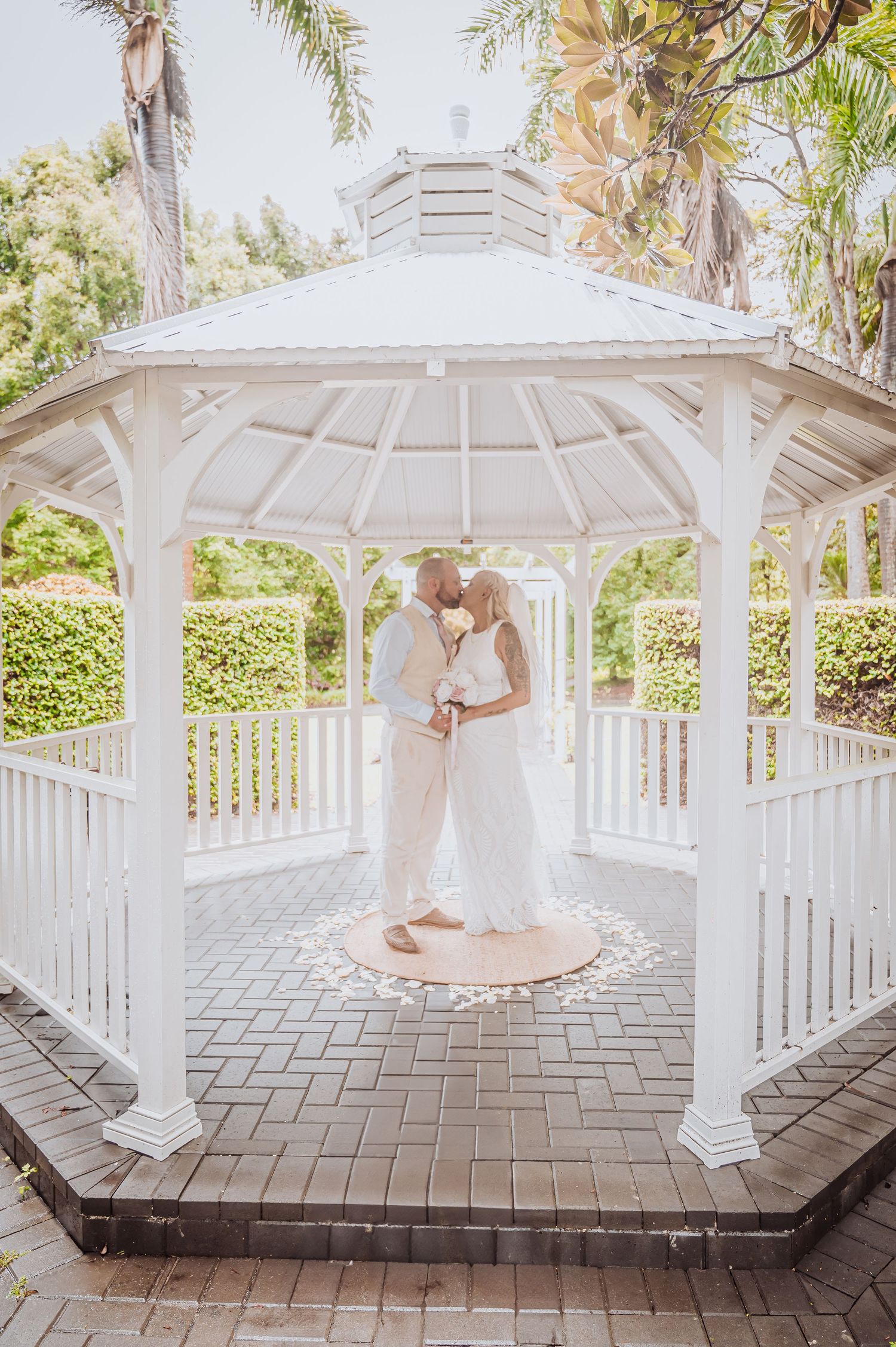 White octagonal gazebo wedding scene with tropical palm trees and landscaping.