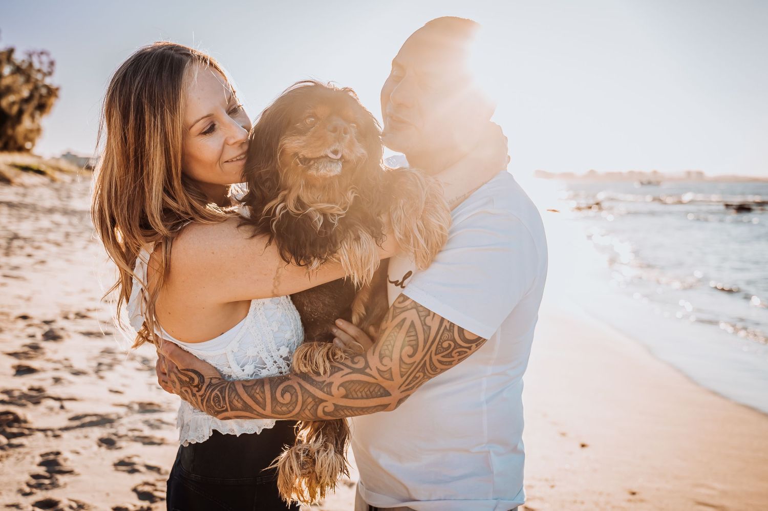 A couple shares a joyful moment with their fluffy brown dog at the beach.