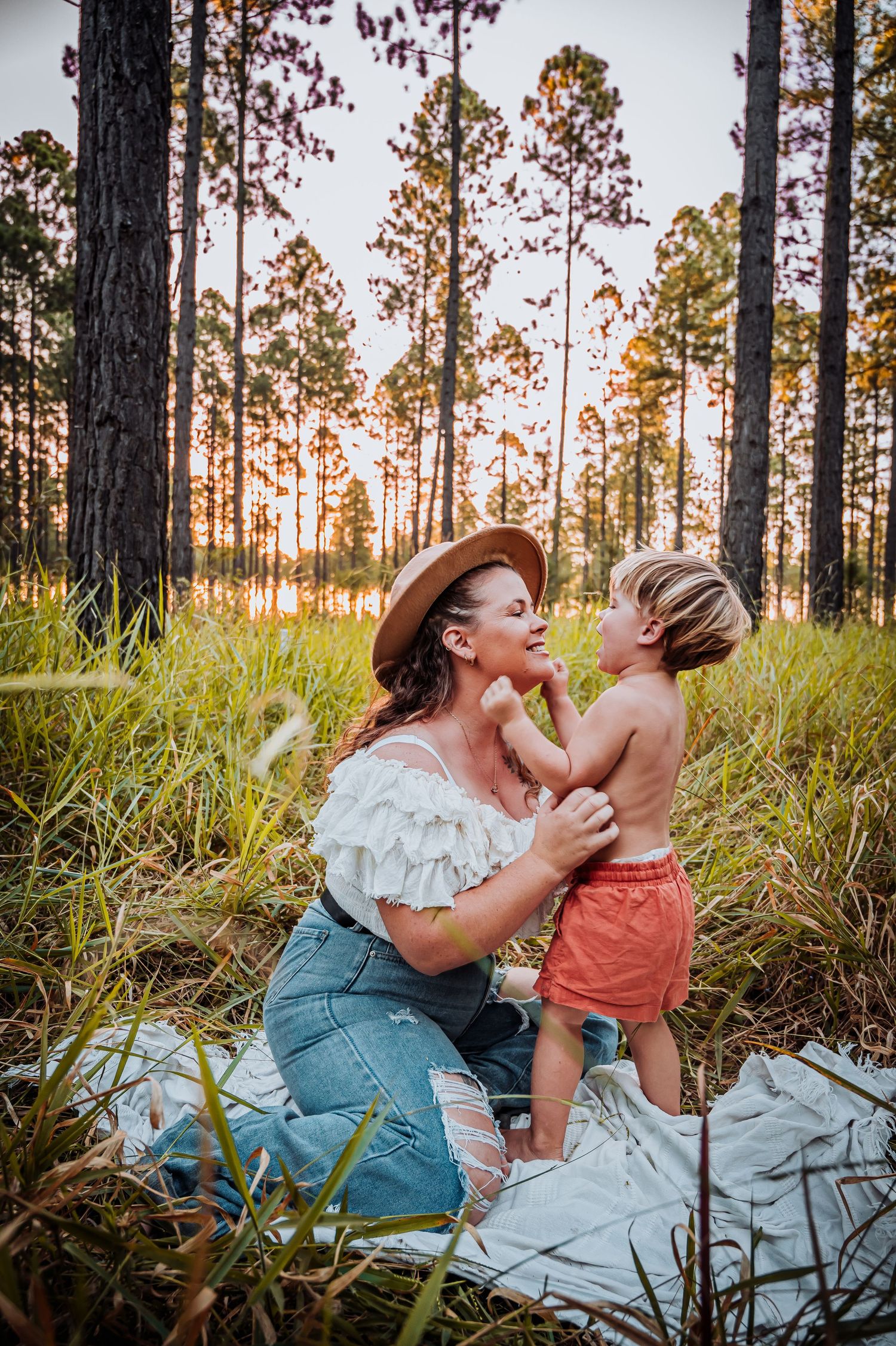 Parent and child sharing a tender moment on a blanket in a pine forest at sunset.