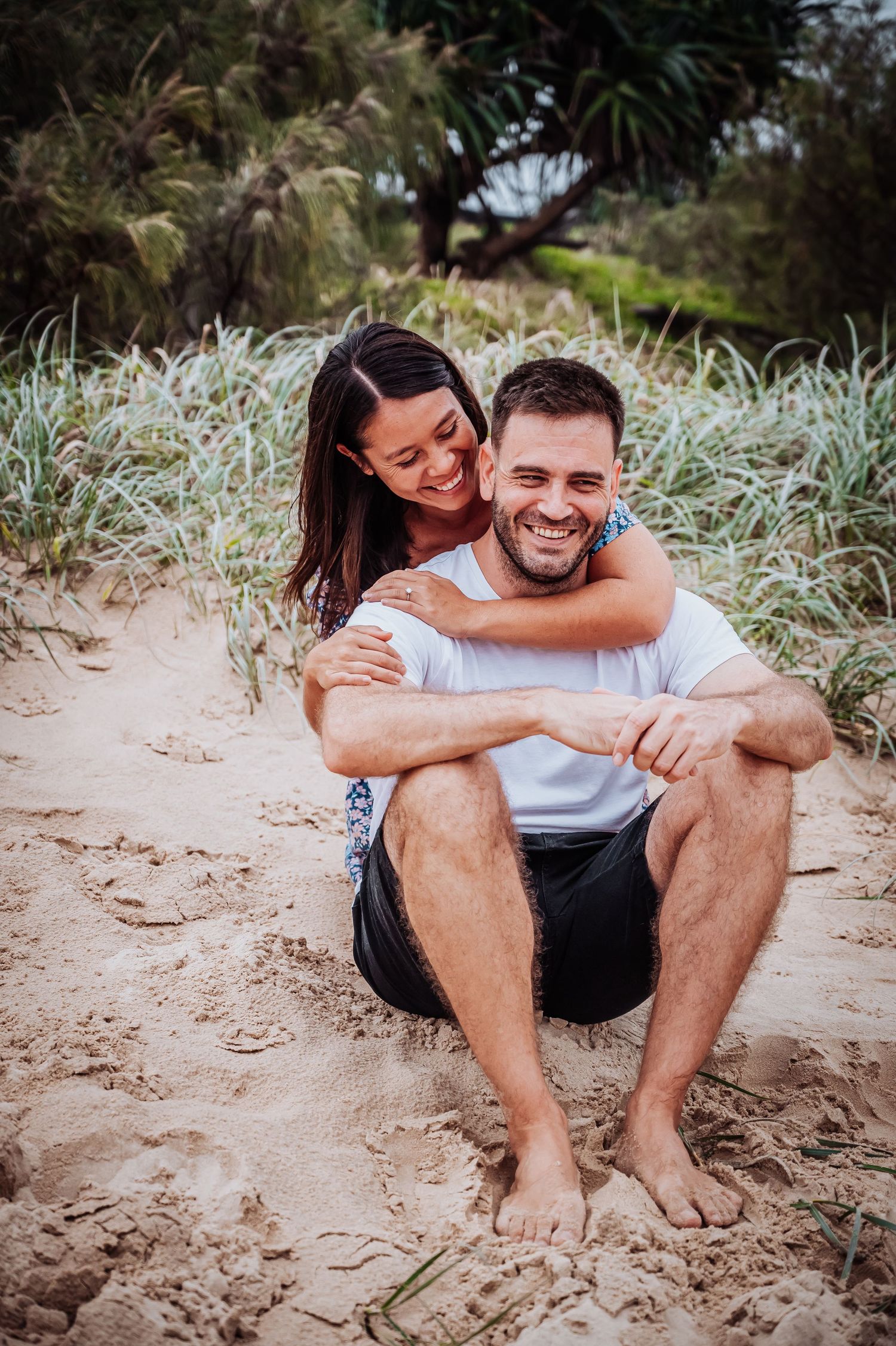 A playful moment shared between a couple sitting in beach grass.