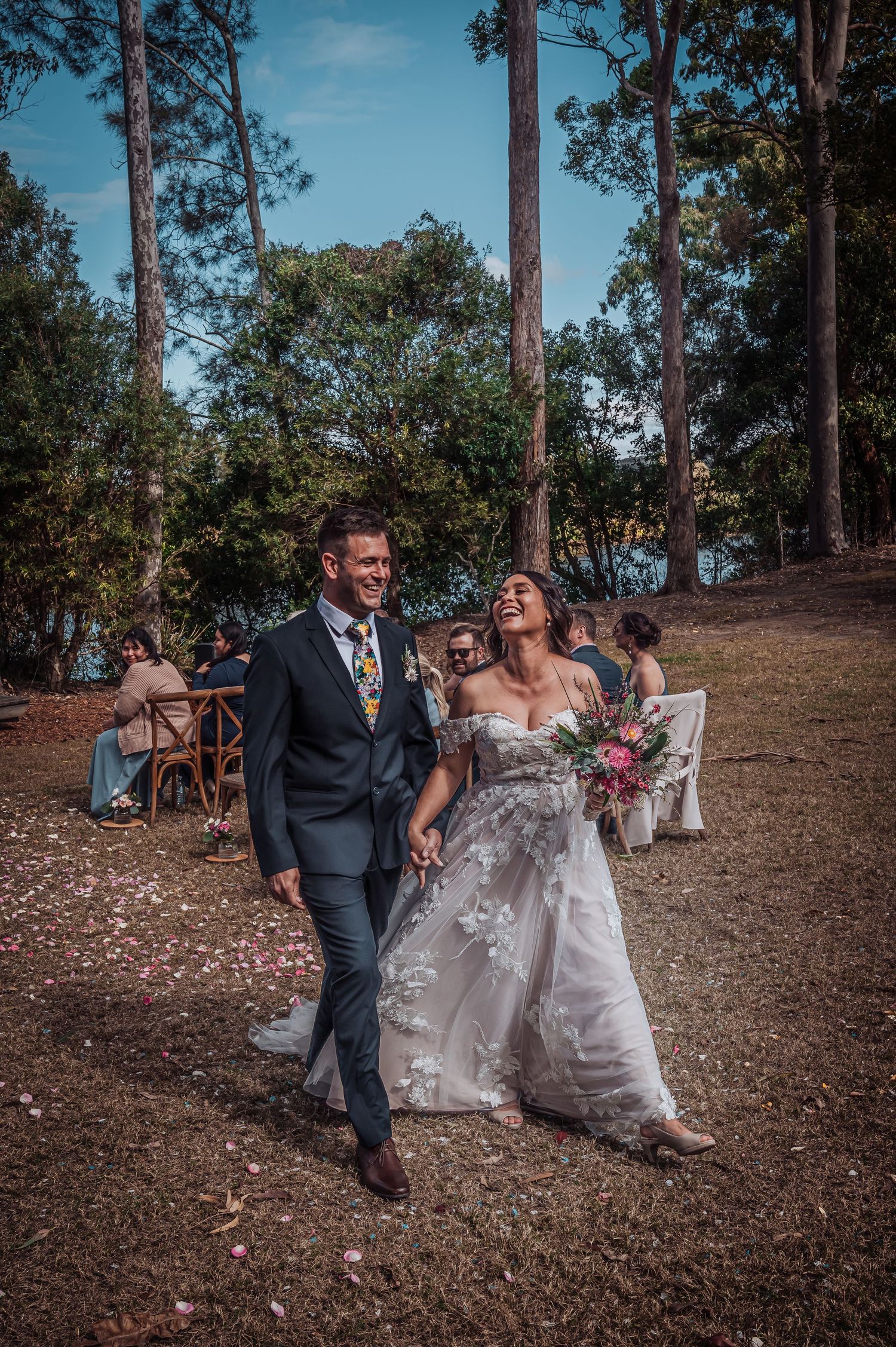 A newlywed couple shares a joyful moment walking together on a woodland path during their outdoor wedding.