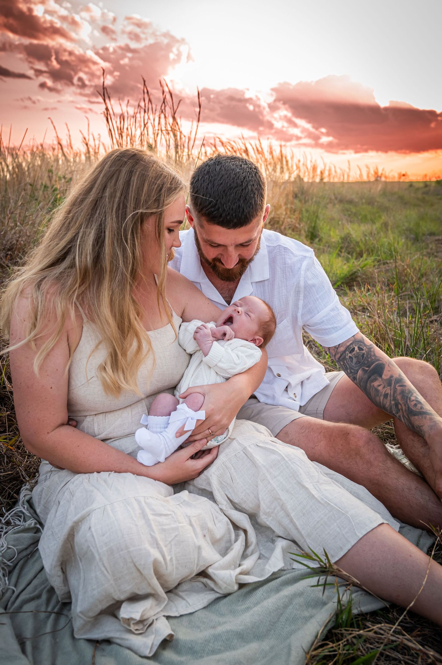 Family sitting on blanket in grass field during sunset photoshoot.