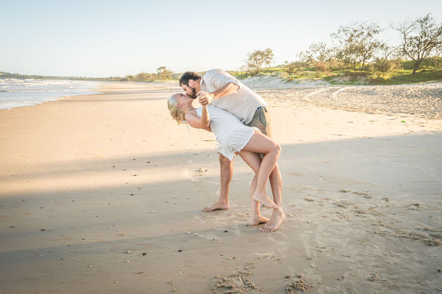 A playful dip pose on a serene beach during sunset.