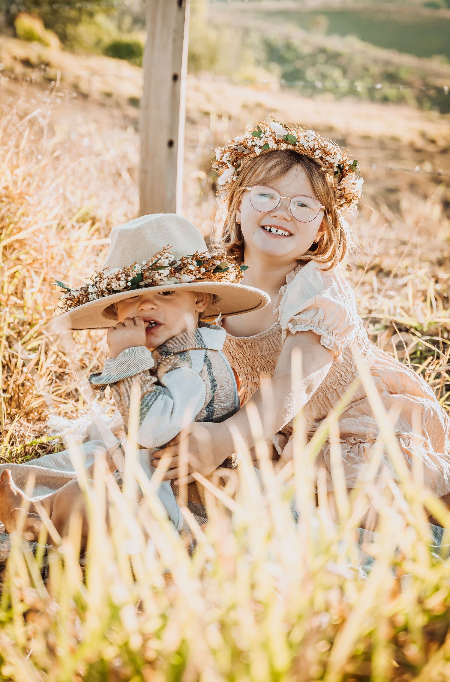 Happy child wearing floral crown and vintage dress sitting in golden field.