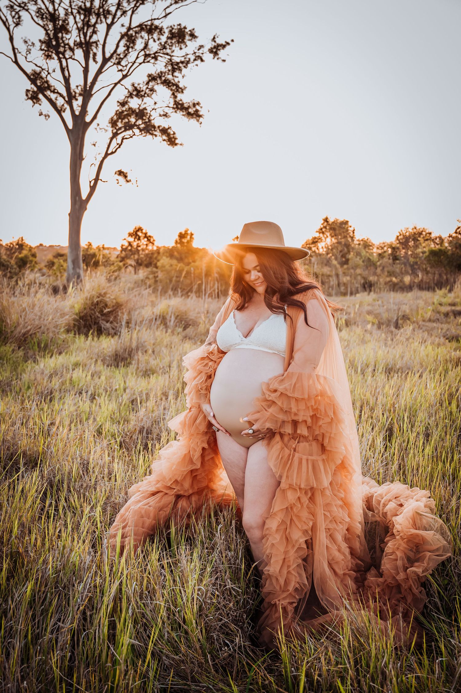 Maternity photo of expectant mother in flowing peach gown at sunset in tall grass.