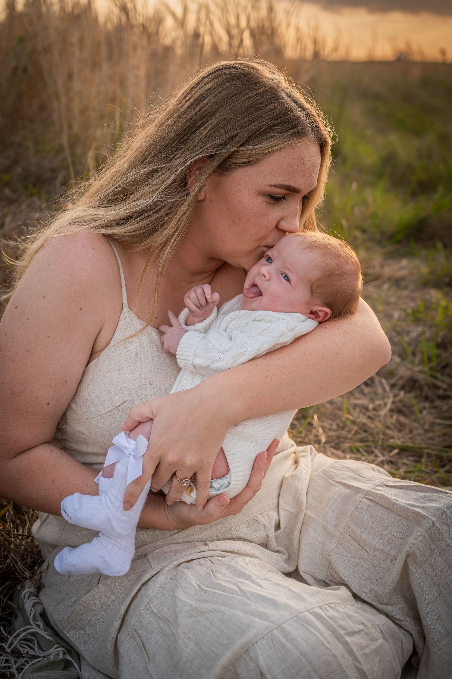 A tender moment captured between a parent and infant outdoors during golden hour in a field.