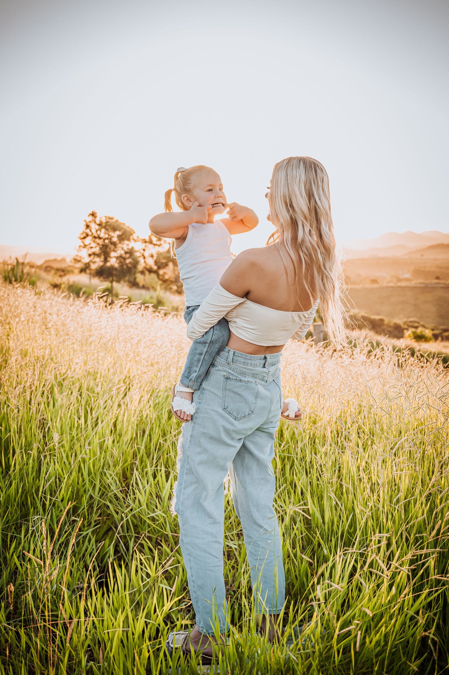 Parent and child sharing a joyful moment in a sunlit field of tall grass.
