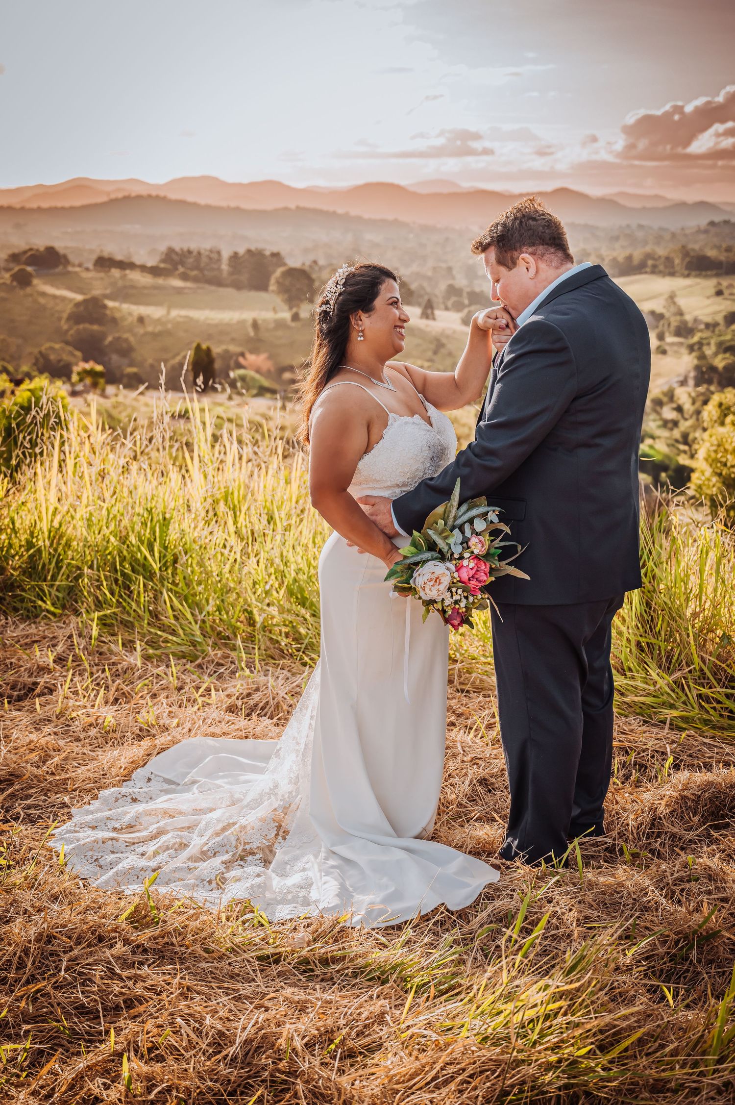 Intimate wedding moment captured in golden field with mountain backdrop at sunset.