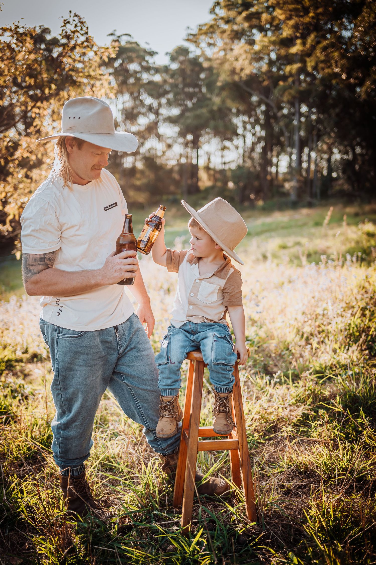 Parent and child in matching hats share playful moment by wooden ladder in sunlit field.