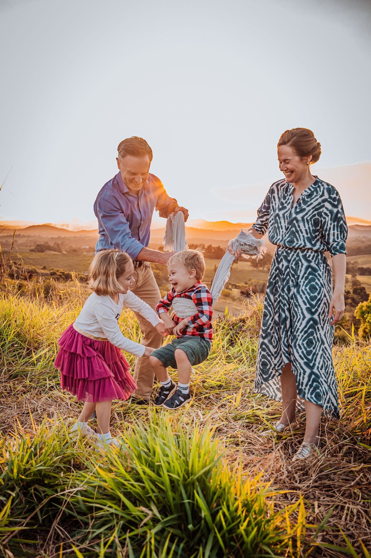 Family playing together outdoors during sunset in tall grass on hillside.