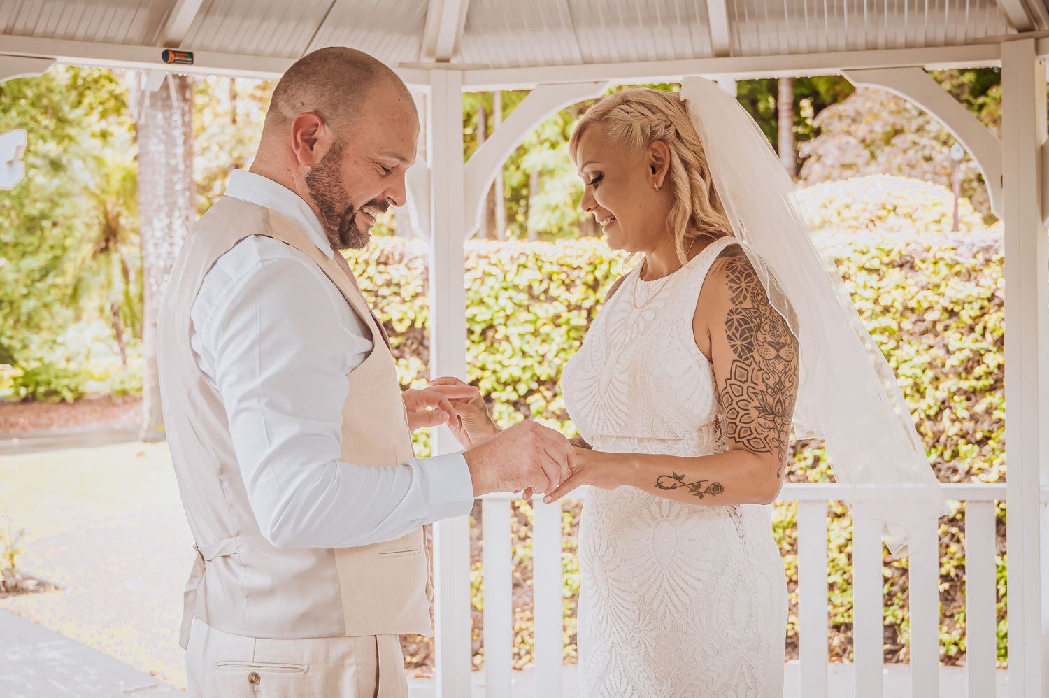 Wedding couple exchanging rings during ceremony in white gazebo.
