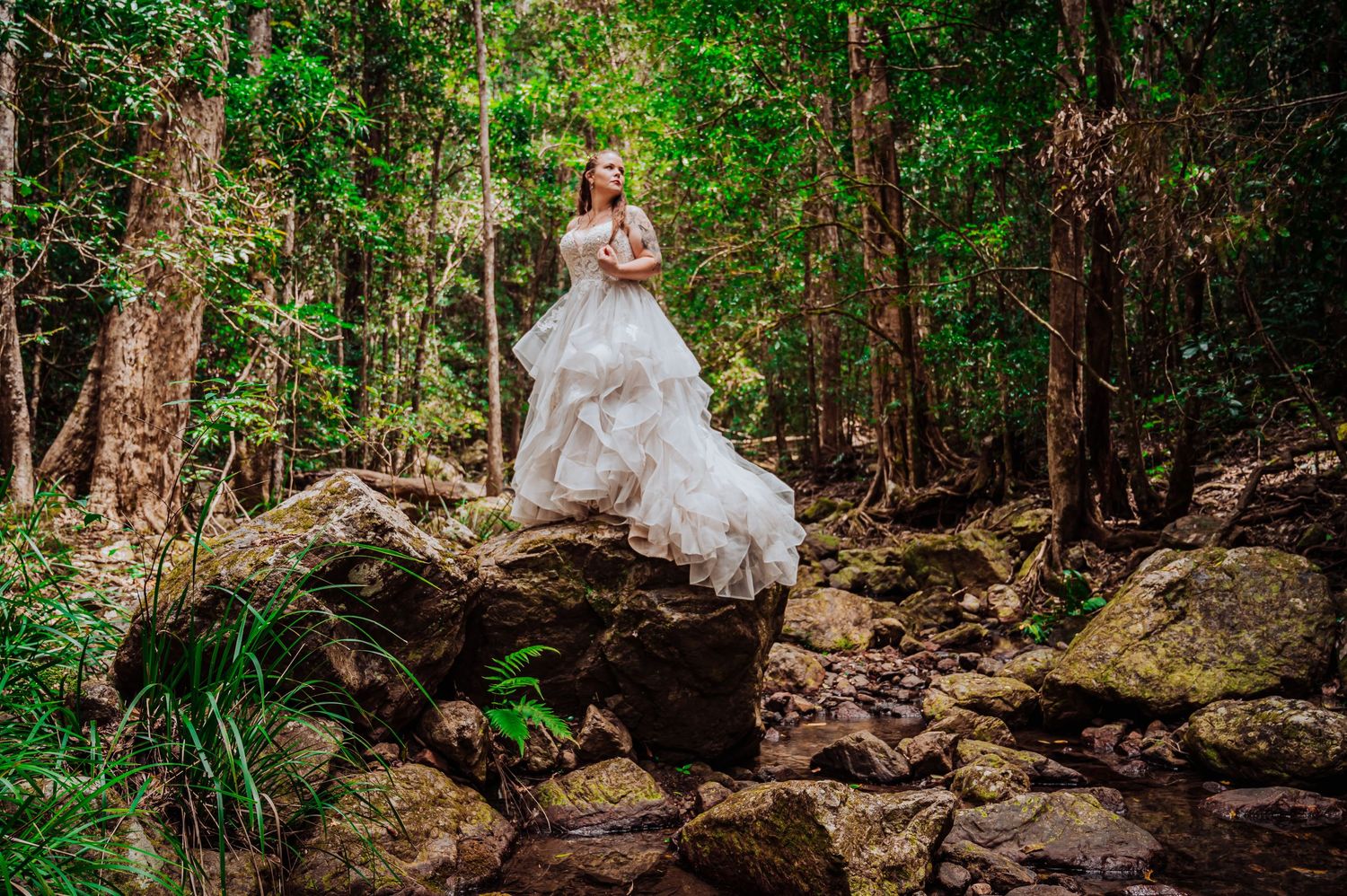 Ethereal bridal portrait on rocky terrain in forest setting with flowing white dress.