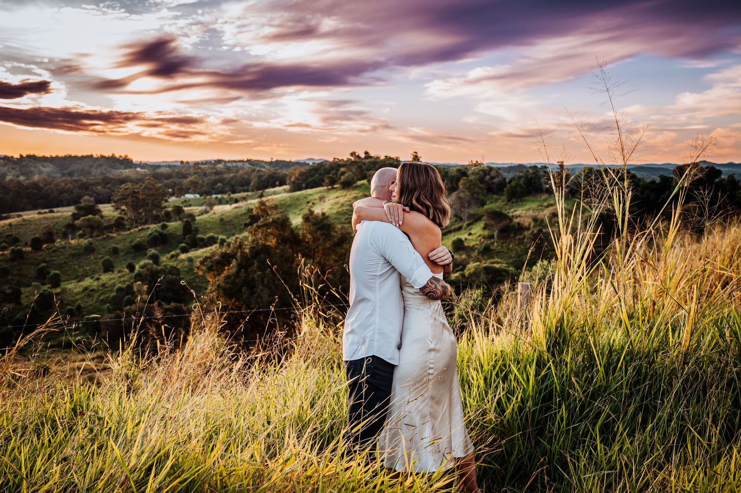A couple shares an intimate moment while overlooking a scenic valley at sunset.