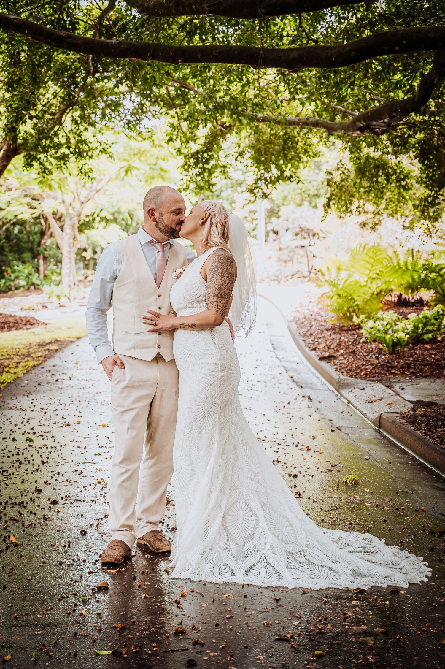 Wedding couple sharing intimate moment on tree-lined garden path.