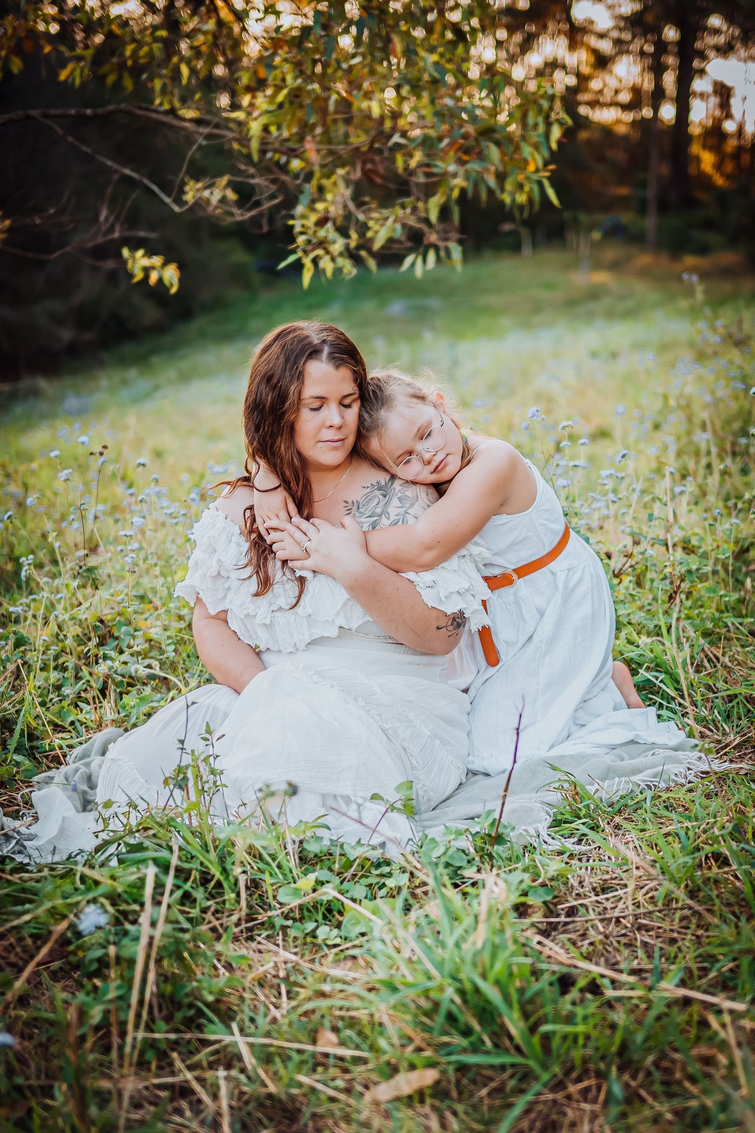 Tender outdoor portrait in white dresses amid tall grass with soft natural lighting.