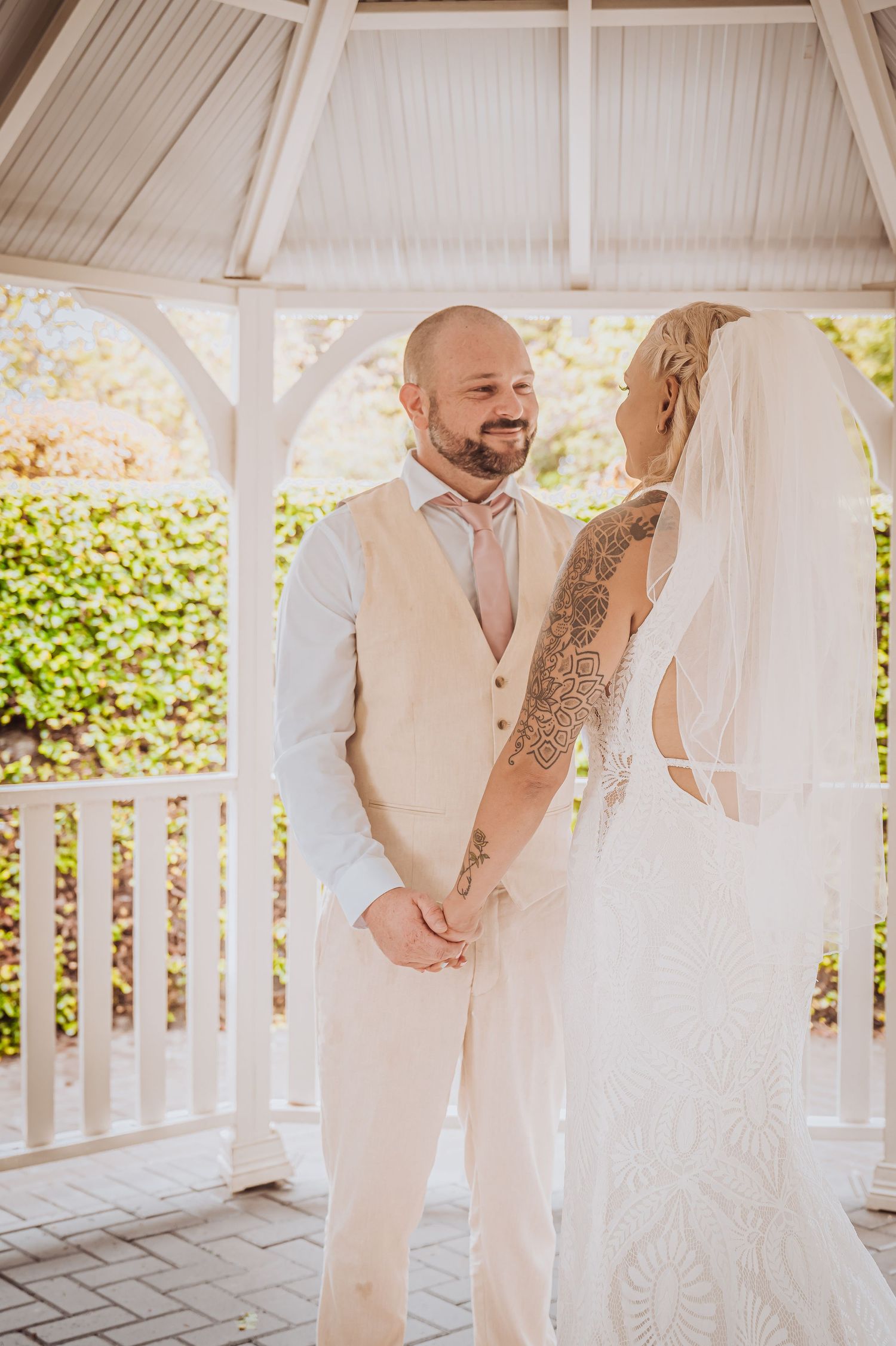 Wedding couple smiling at each other while standing in an elegant white gazebo setting.