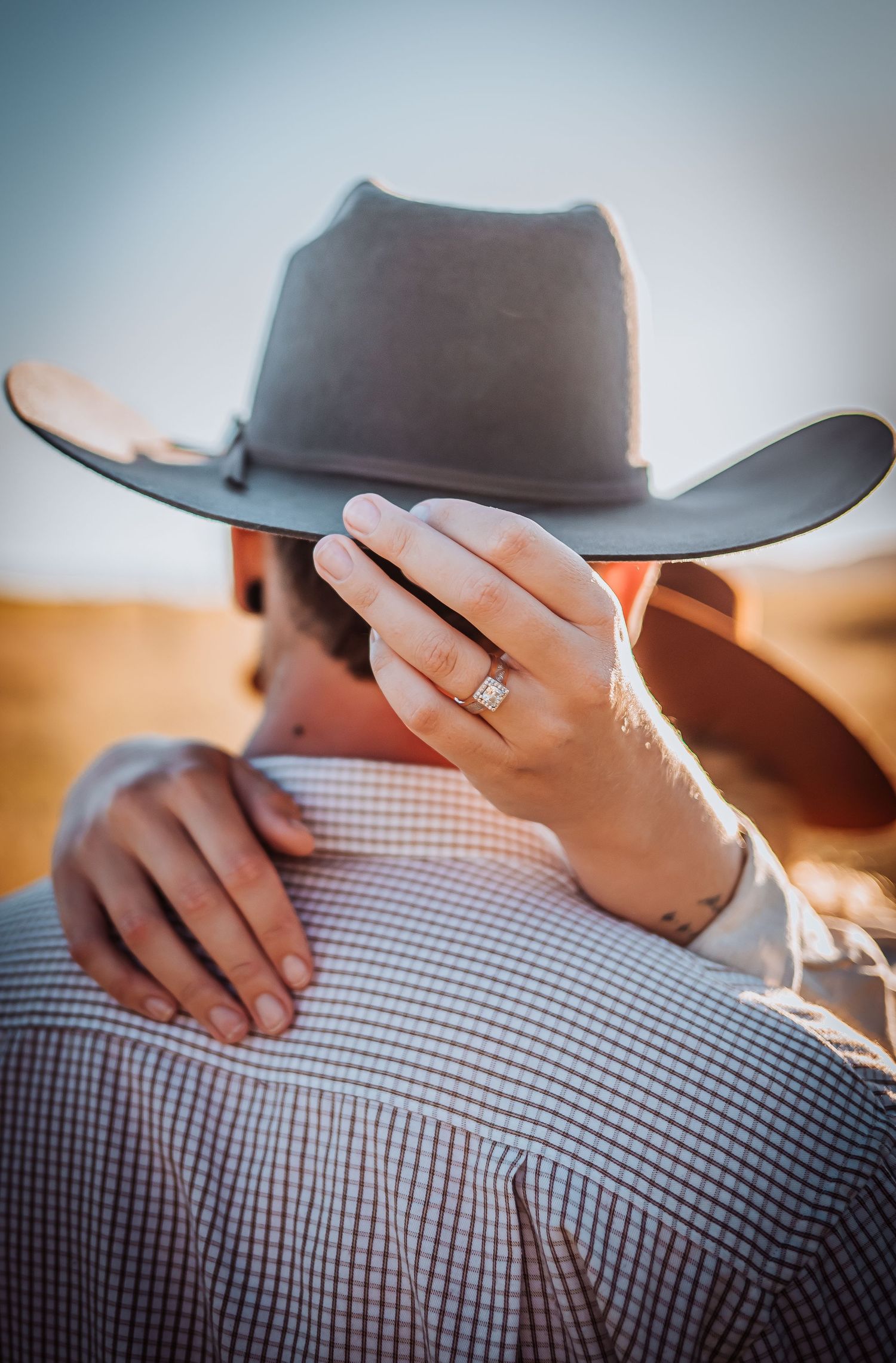 Close-up of a cowboy hat and wedding ring with a checkered shirt in soft focus.