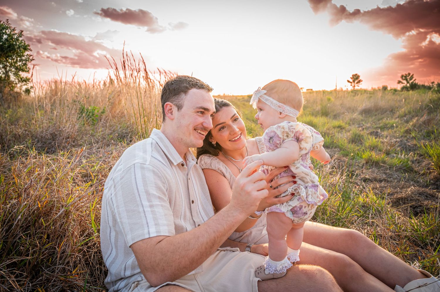 Family sitting together in sunset-lit field wearing coordinated white outfits.