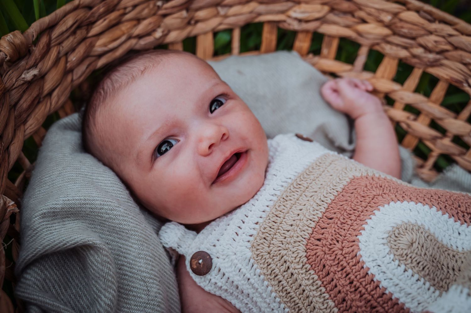 A smiling baby wearing a cream striped sweater relaxes in a woven basket.