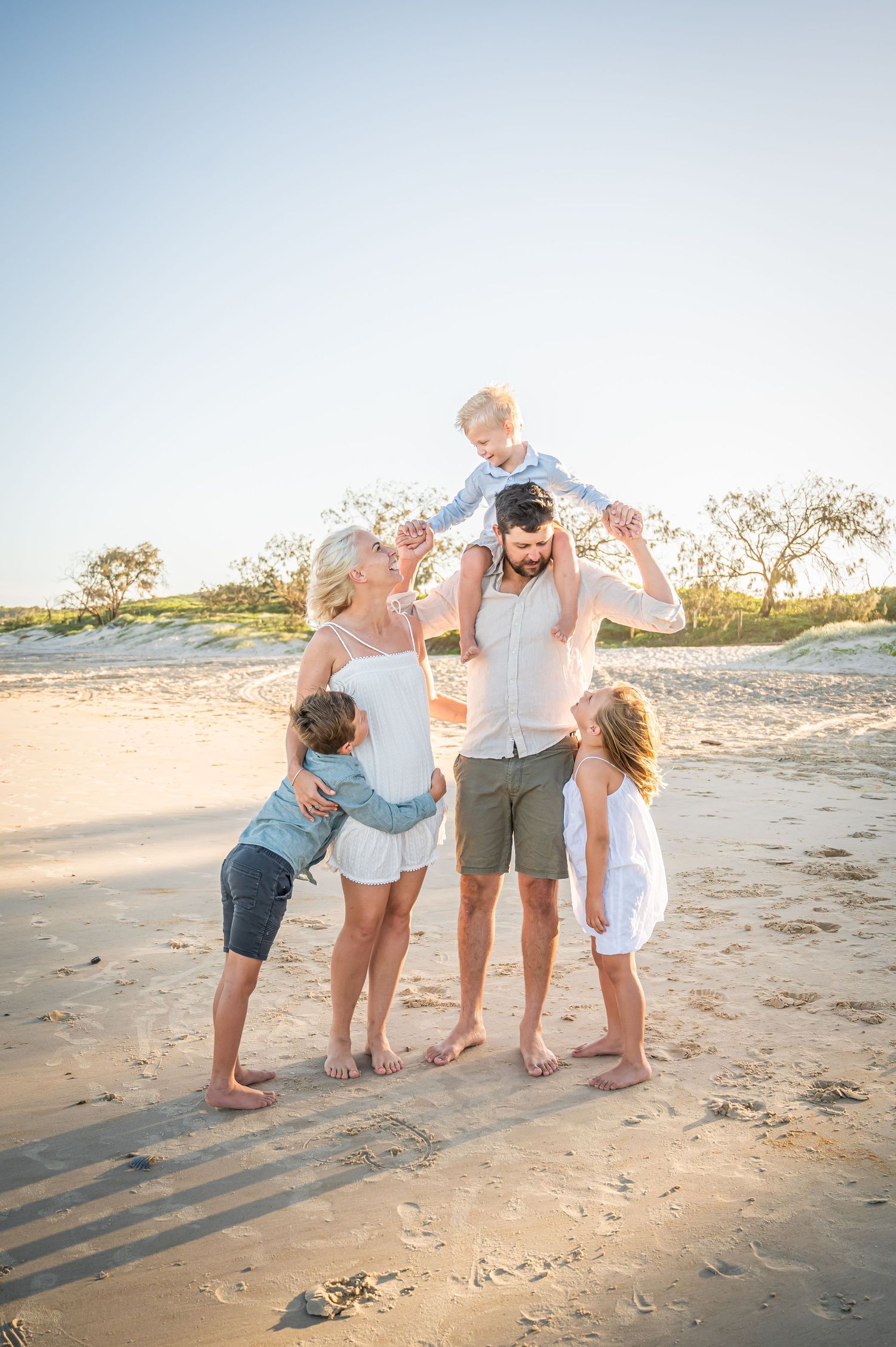 Family enjoys playful moment on beach during sunset with beautiful coastal scenery.
